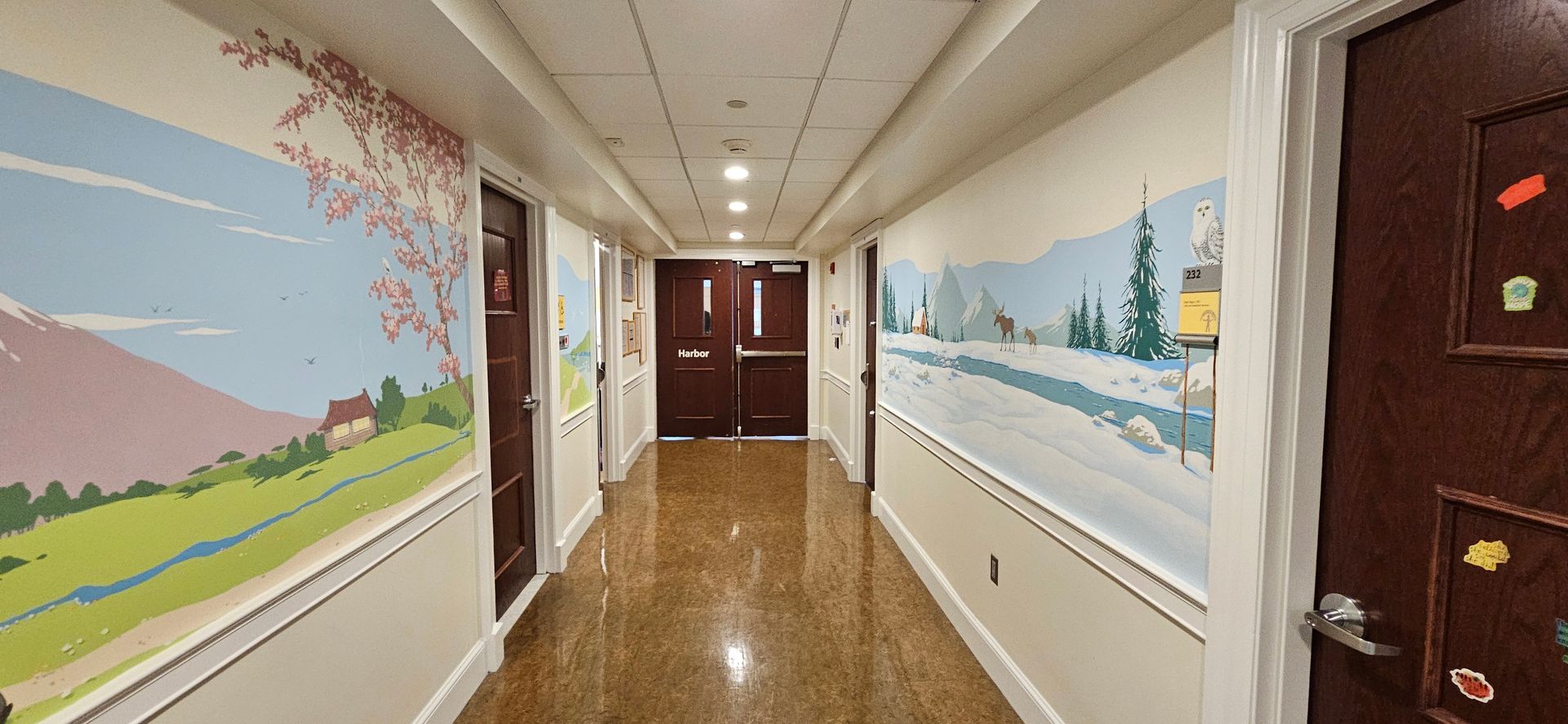 Bright hallway with colorful murals on both walls and polished wood floors leading to double doors.
