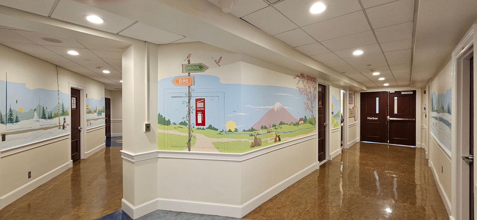 Bright school hallway with murals on the walls, glossy floors, and double doors at the end.