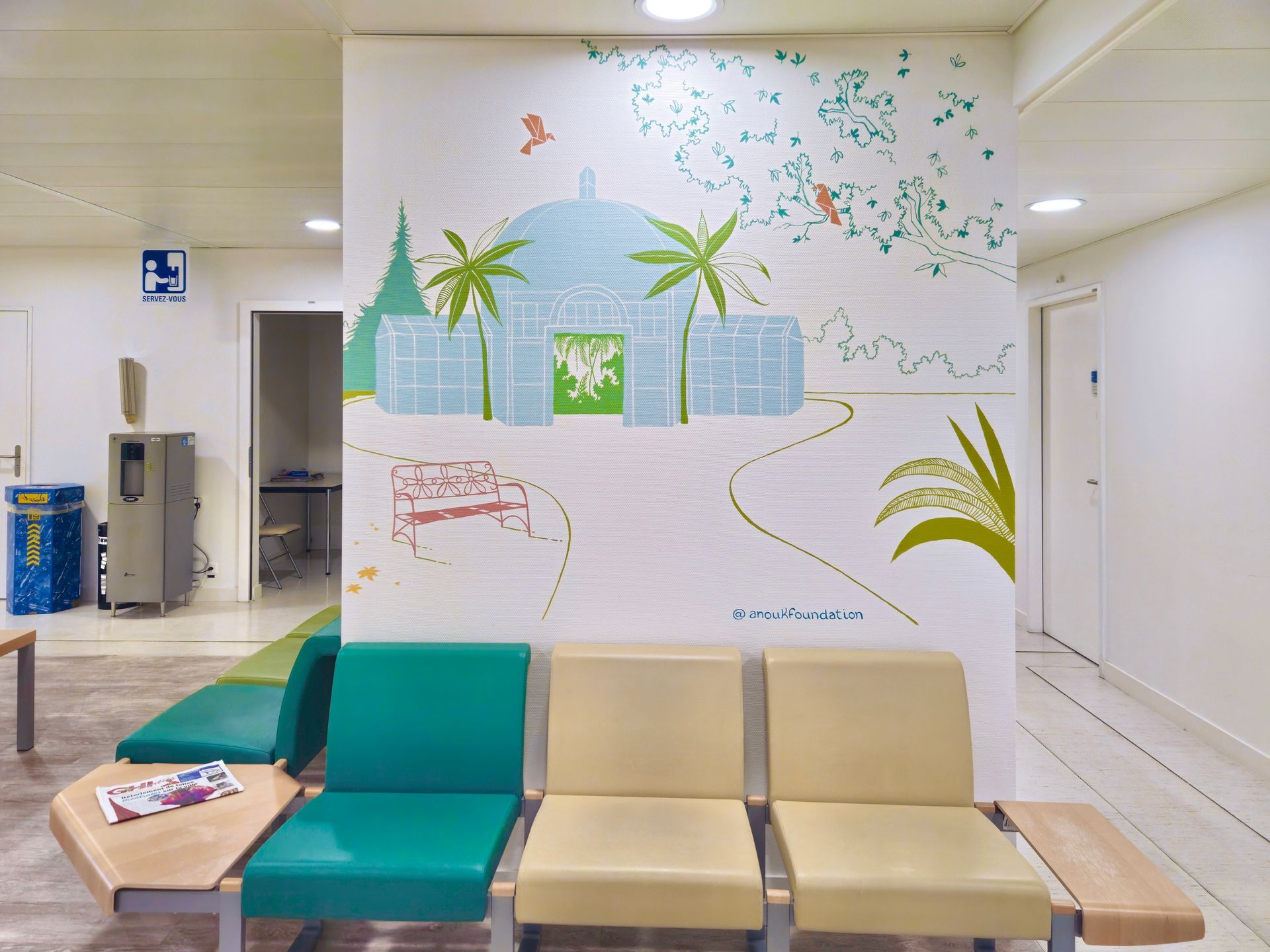 Hospital waiting area with teal and beige chairs and a colorful wall mural.