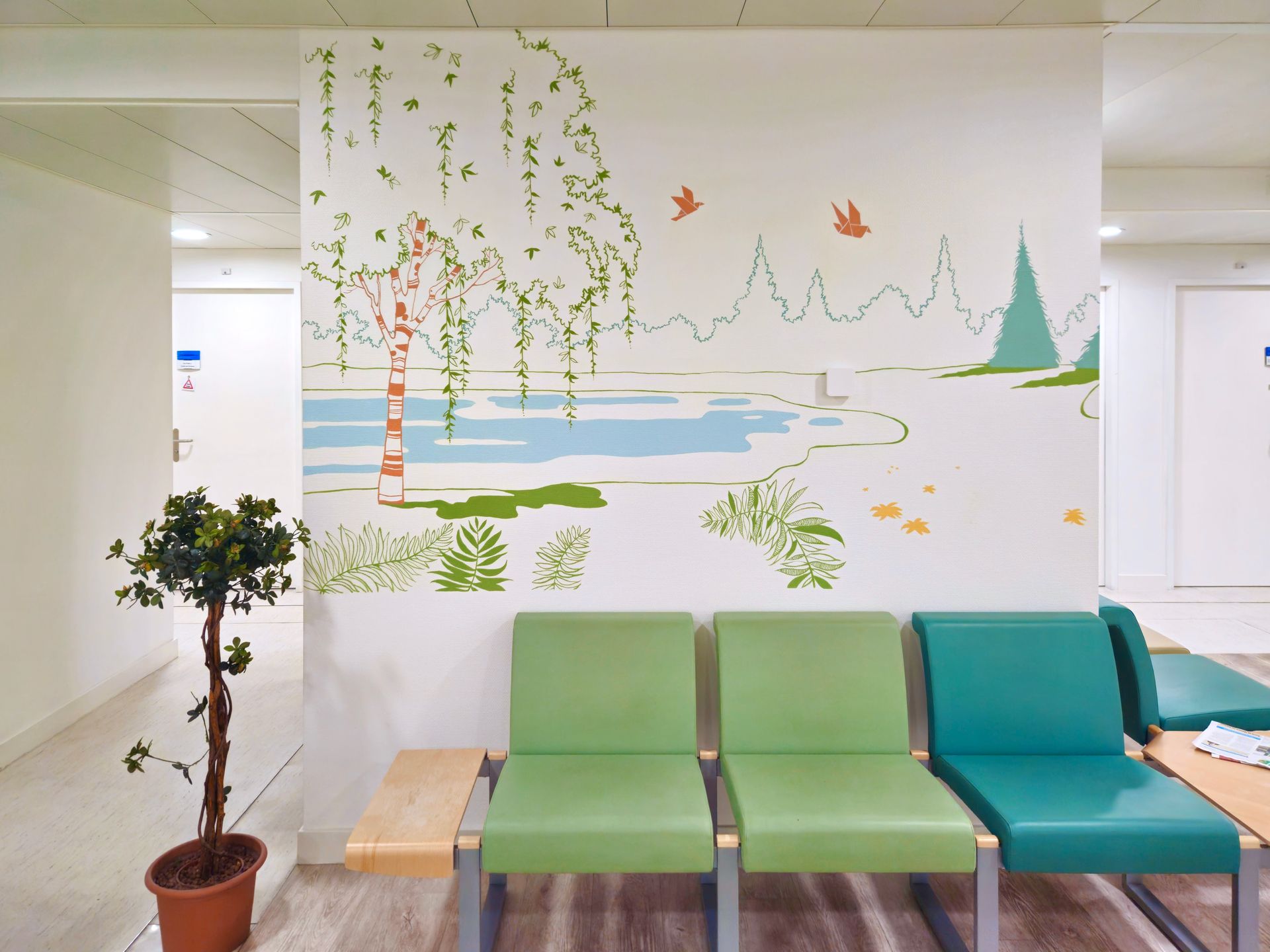 Waiting area with green and teal chairs beneath a wall mural of trees, birds, and a lakeside scene
