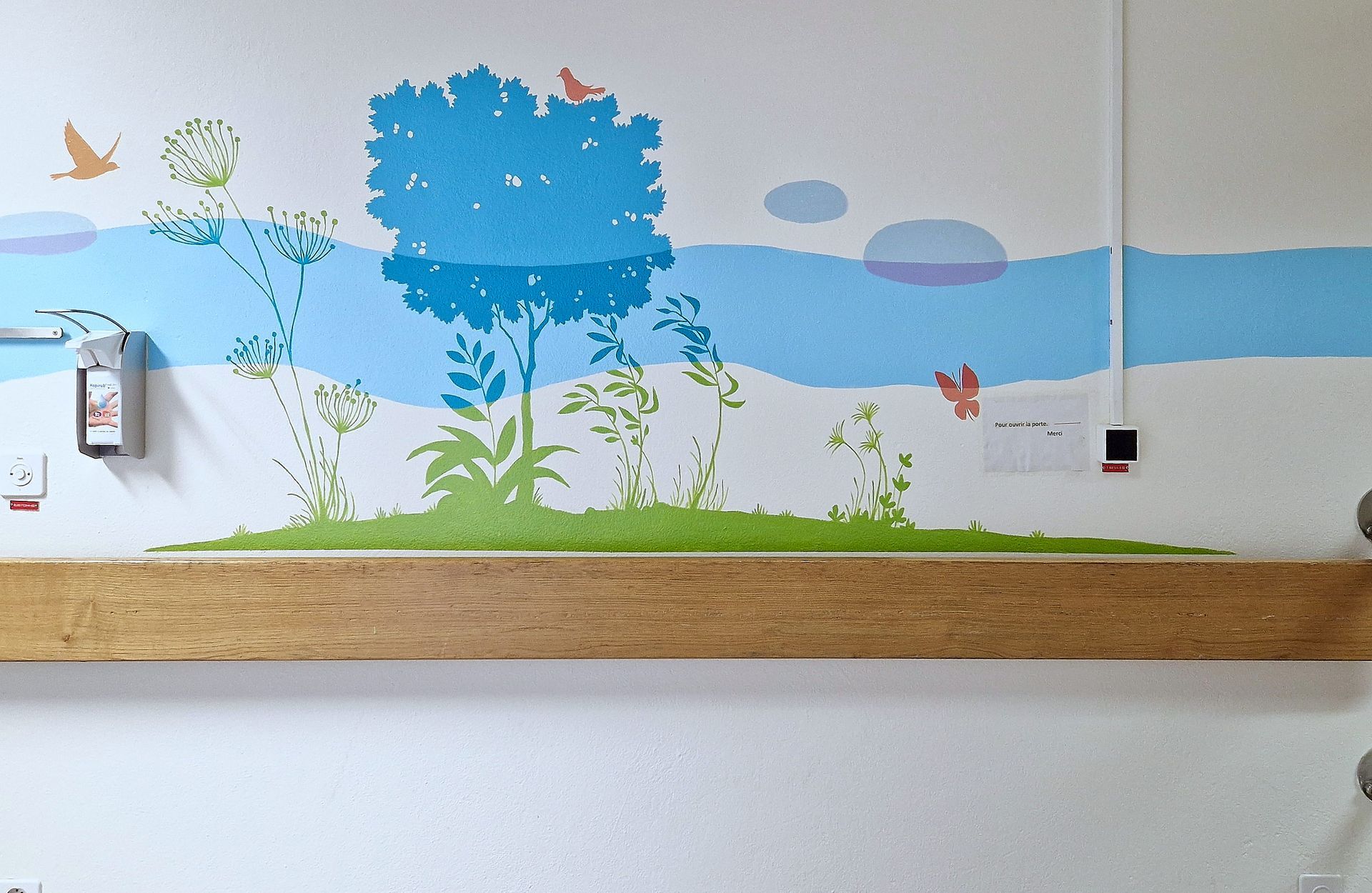 Childlike mural with a blue tree, green grass, clouds, butterflies, and wall fixtures on a white wall