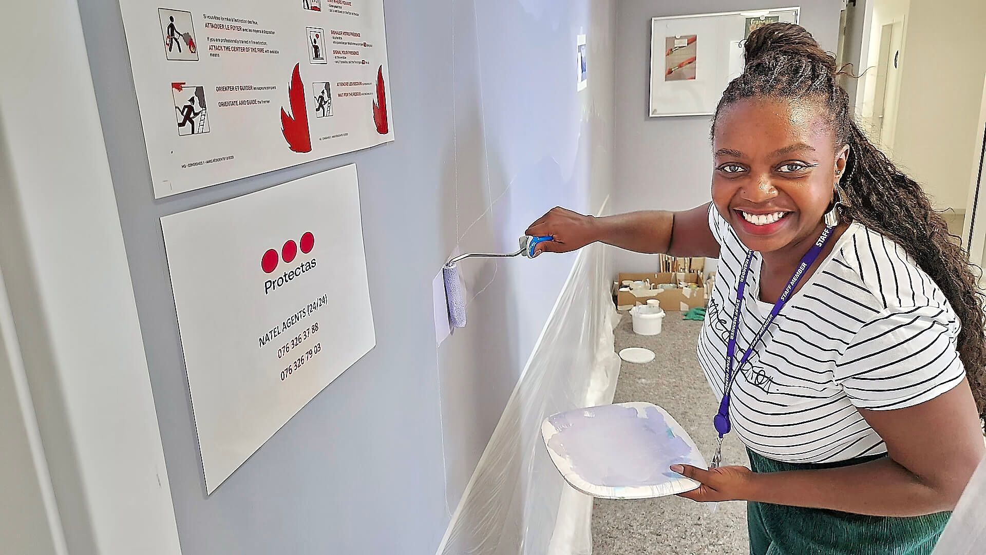 Woman smiling and pointing at wall notices while holding papers in a hallway