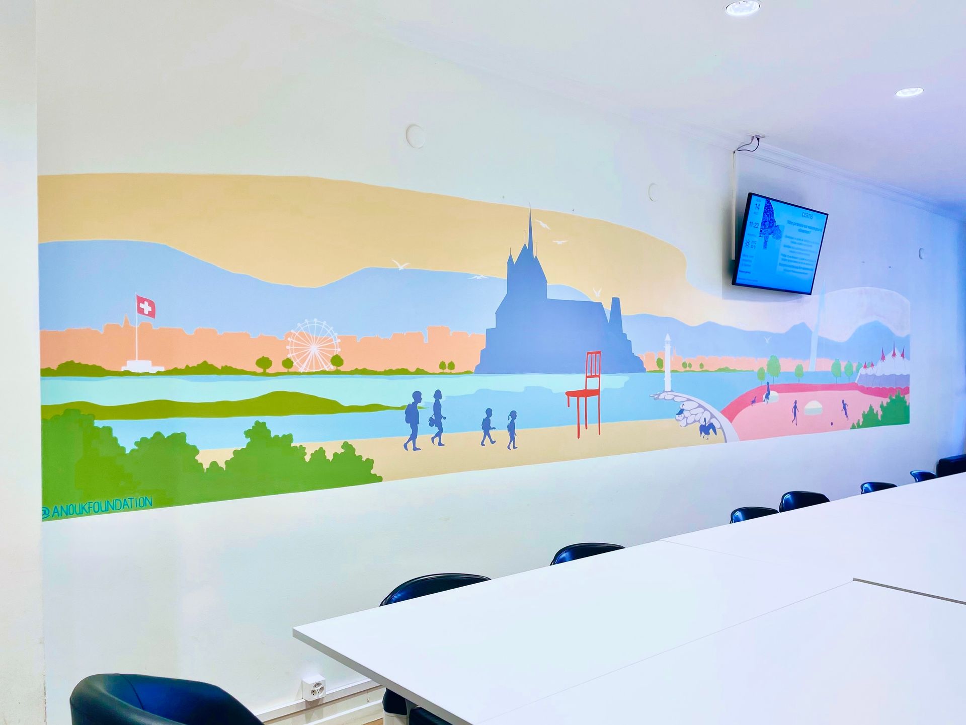 Colorful wall mural in a meeting room above a long white table and chairs, with a TV on the right.