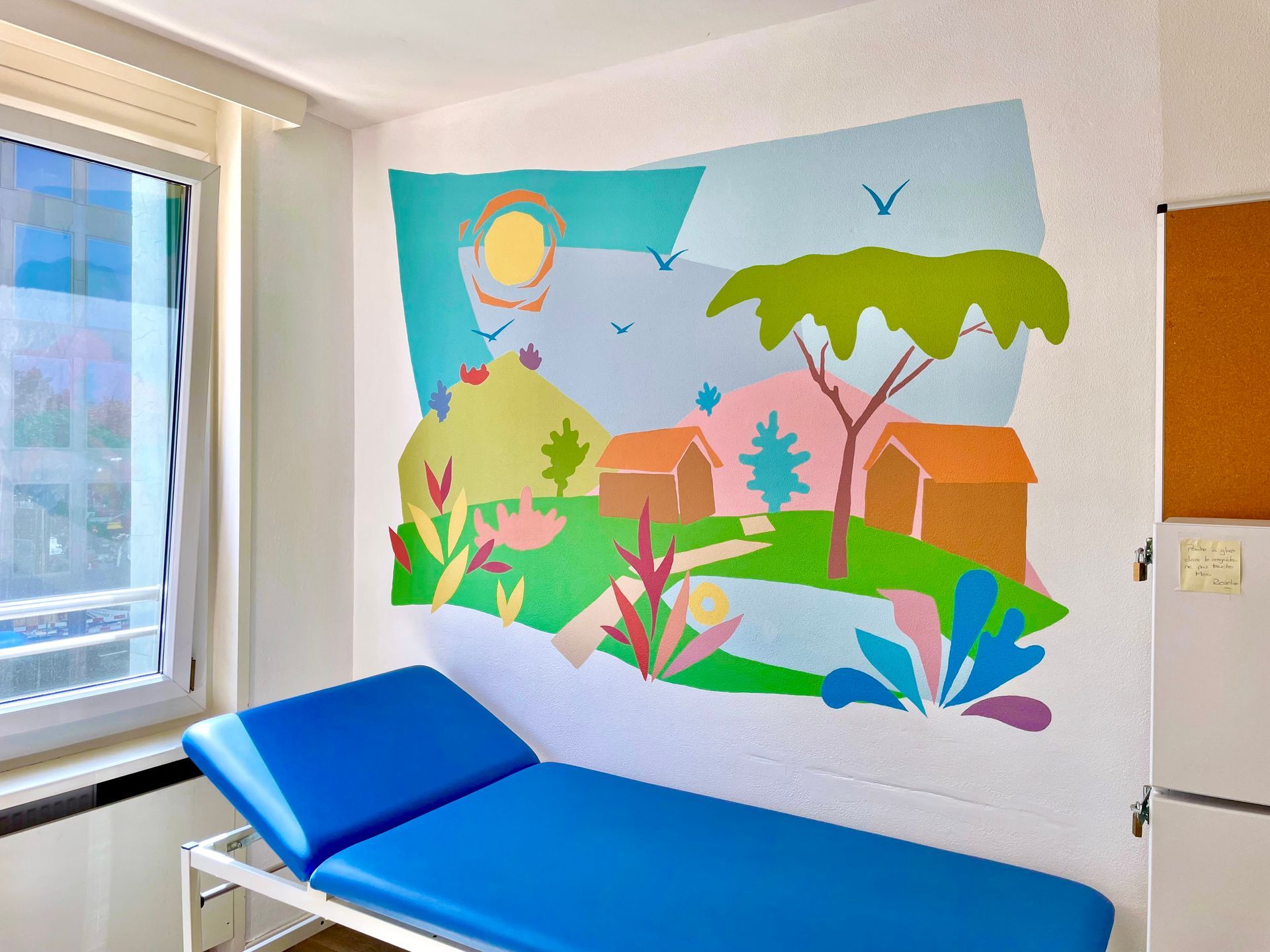 Bright tropical mural in a medical room beside a blue exam table and window