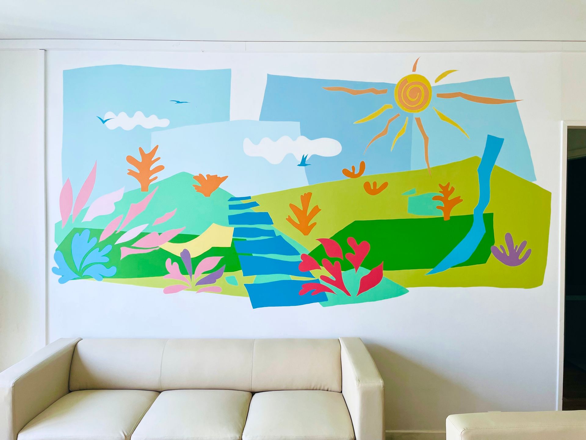 Colorful underwater mural with fish, sea plants, sun, and clouds above a white couch