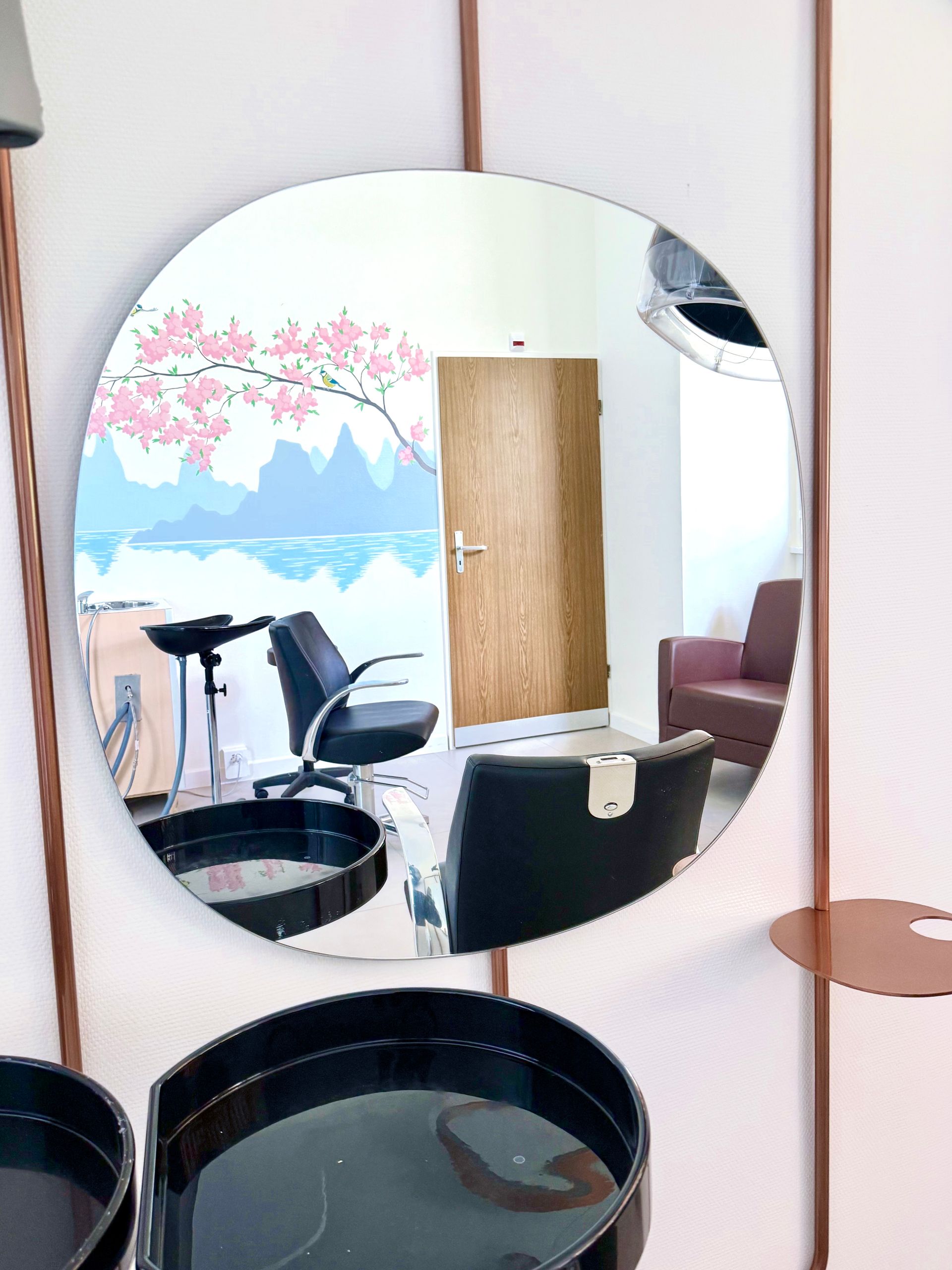 Round mirror reflecting a small room with a bike, chair, wooden door, and mural wall art