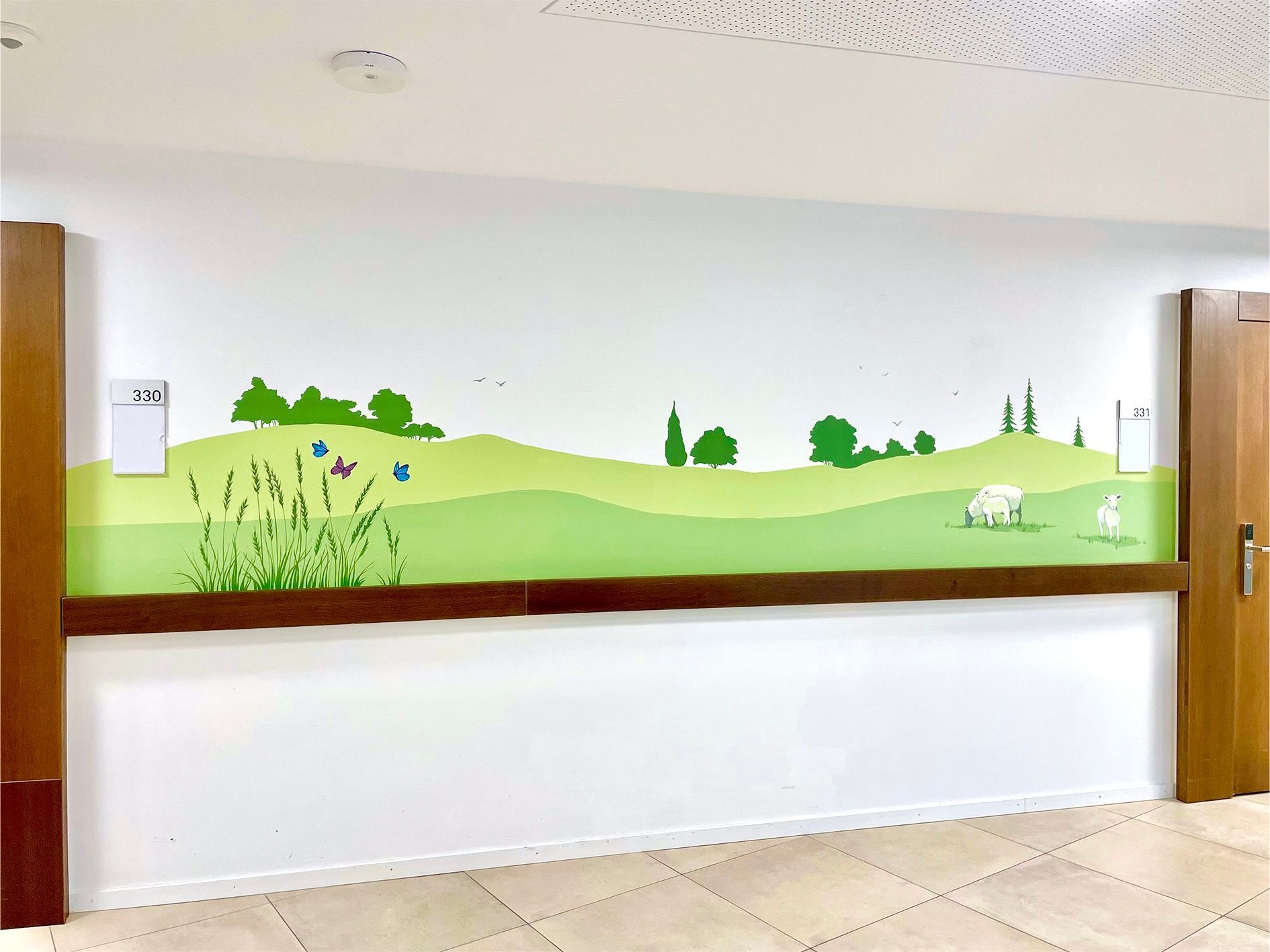 Wall mural of green hills, trees, and a sheep above a white bench in a bright hallway
