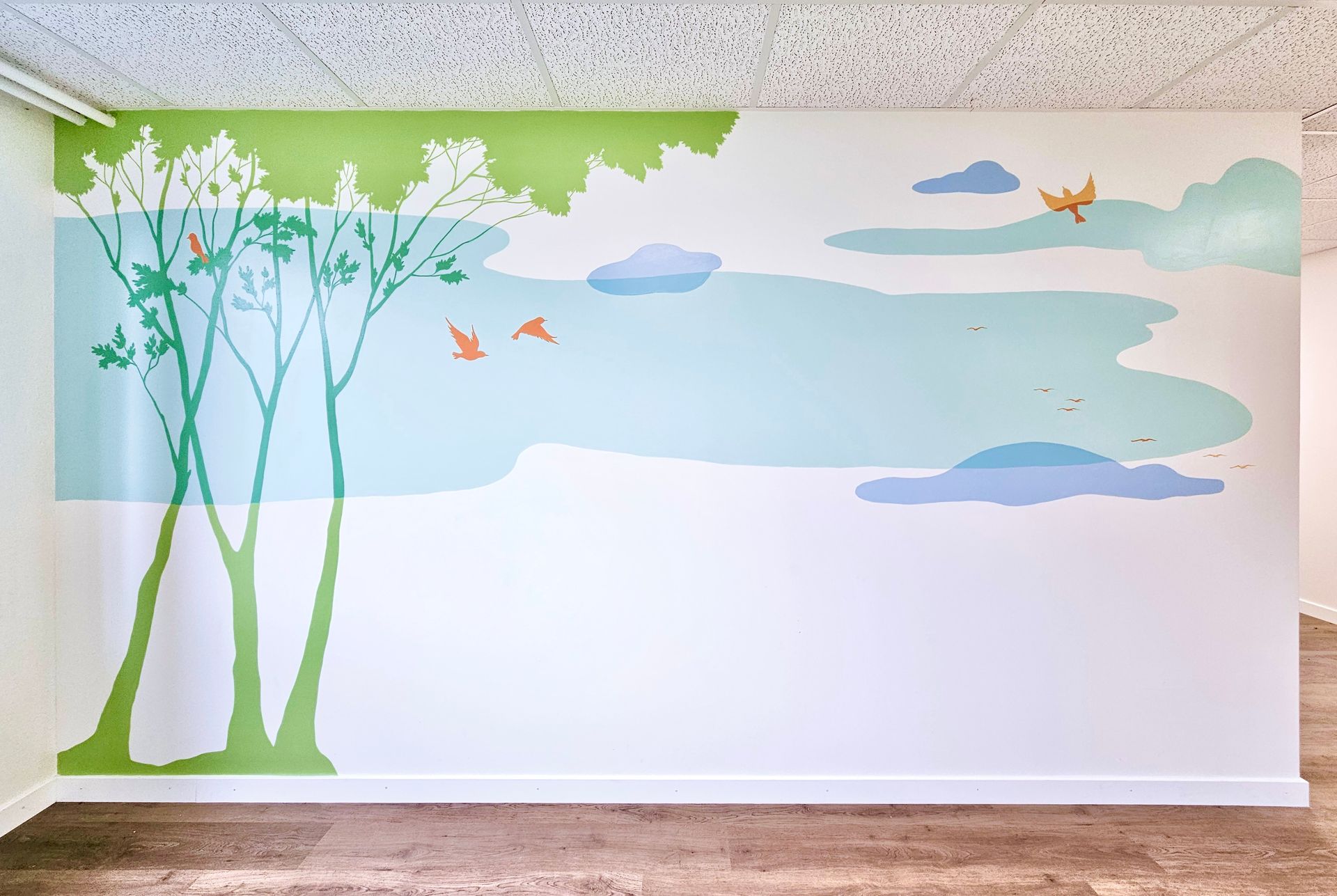 Wall mural with green trees, birds, clouds, and a blue sky above a blank white lower wall