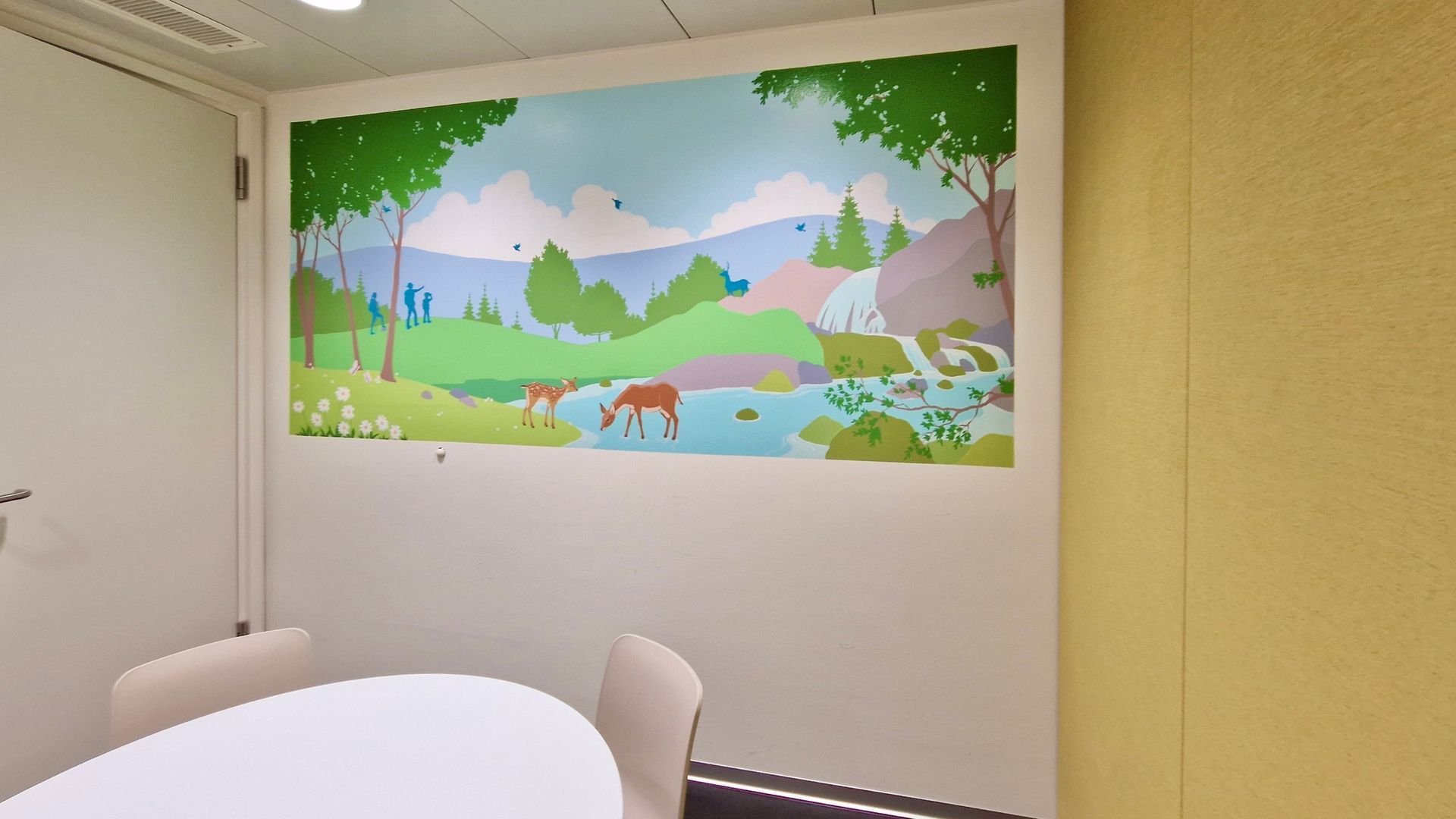 Meeting room with round table and chairs, featuring a colorful mural of a deer, lake, trees, and mountains.