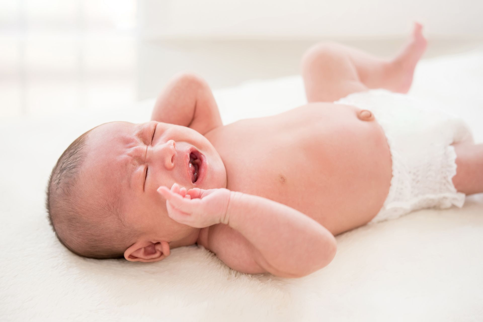 A baby in a diaper is crying while laying on a bed.