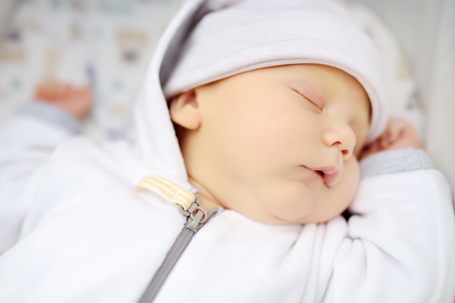 A newborn baby is sleeping in a white blanket and hat.