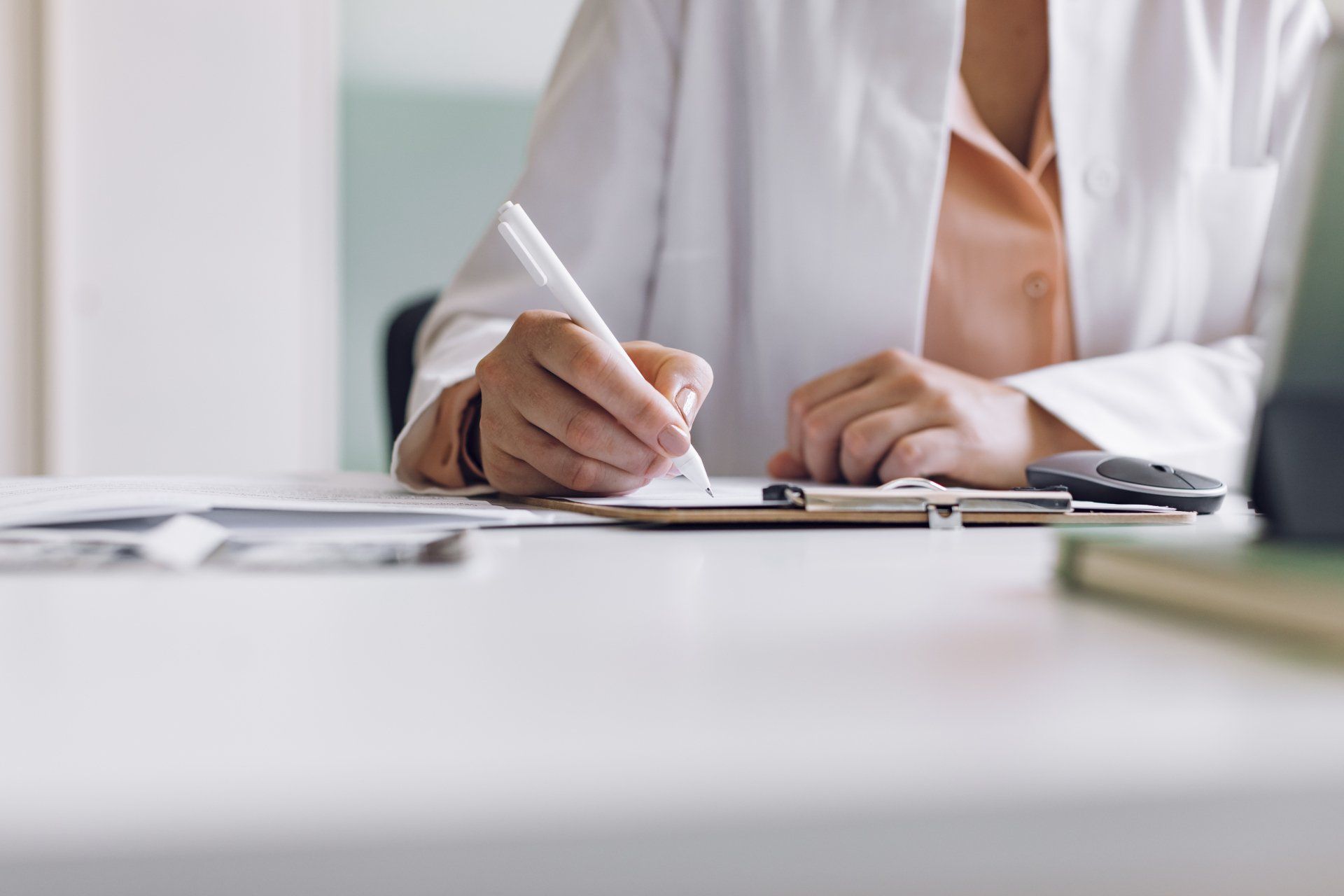 A doctor is writing on a clipboard with a pen.
