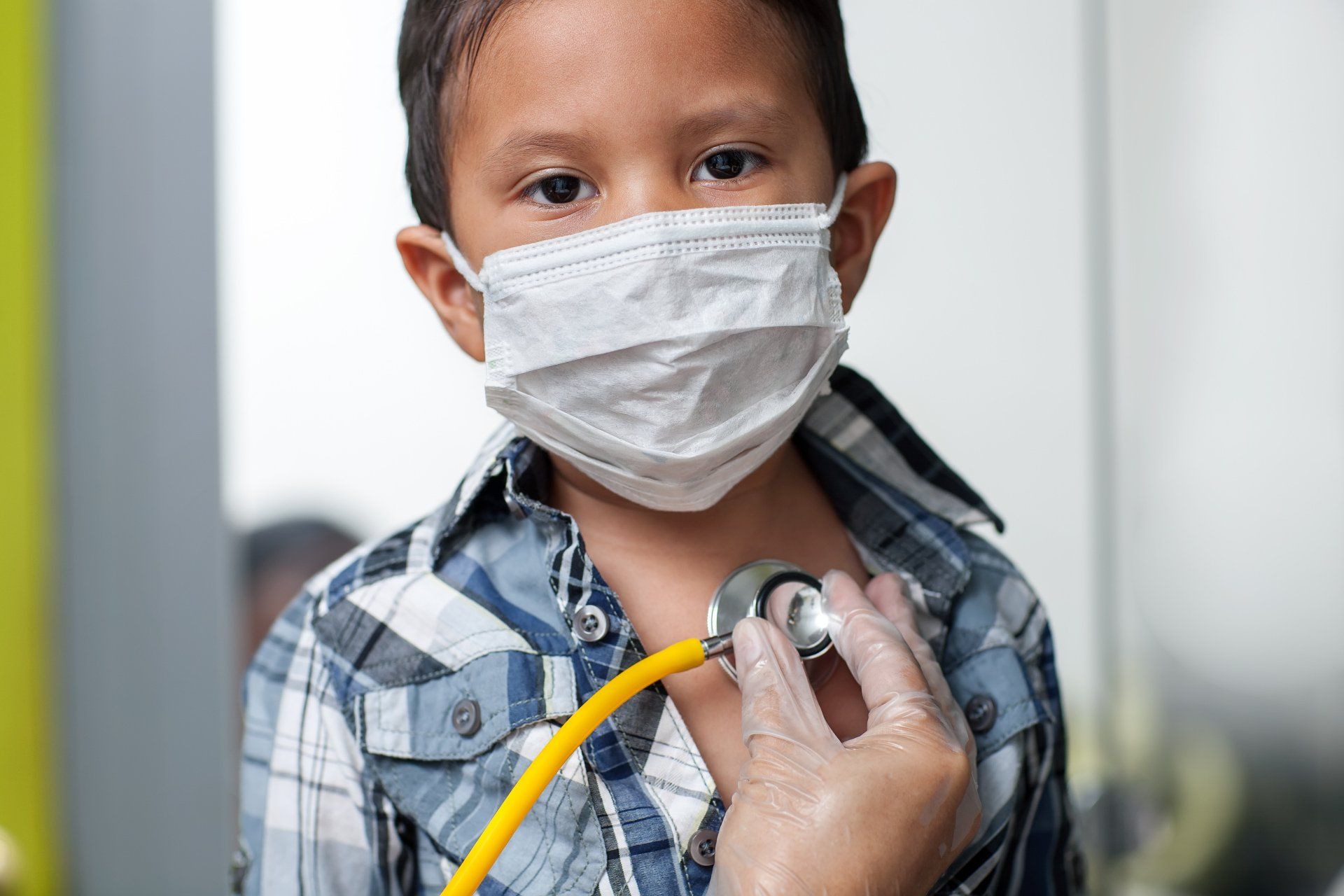A young boy wearing a mask is being examined by a doctor with a stethoscope.