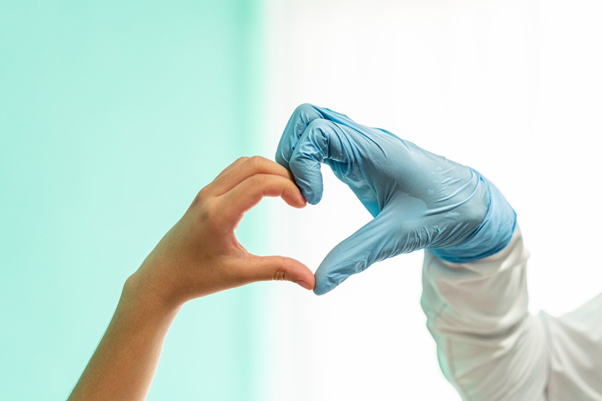 A person wearing blue gloves is making a heart shape with their hands.