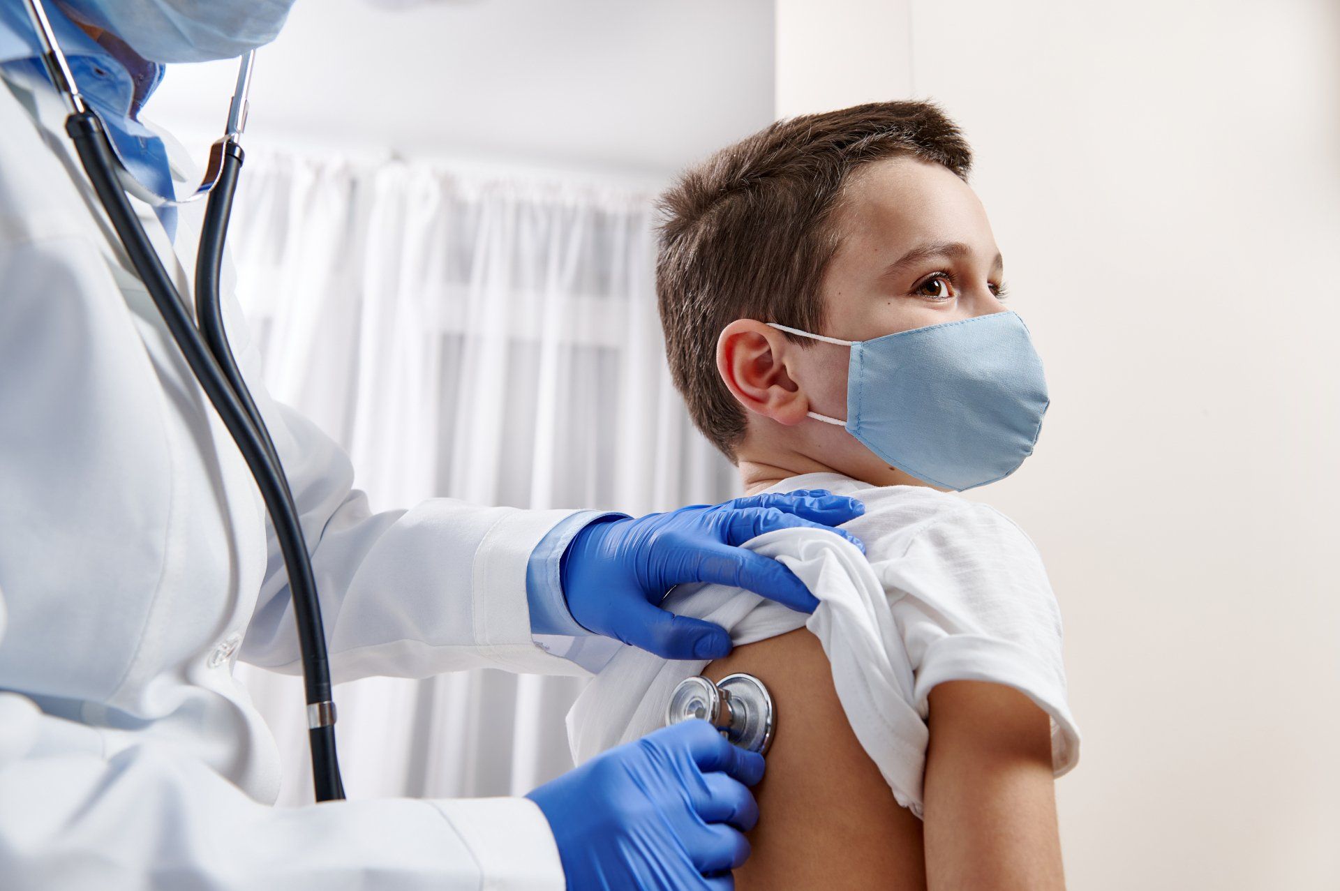 A young boy wearing a mask is being examined by a doctor with a stethoscope.