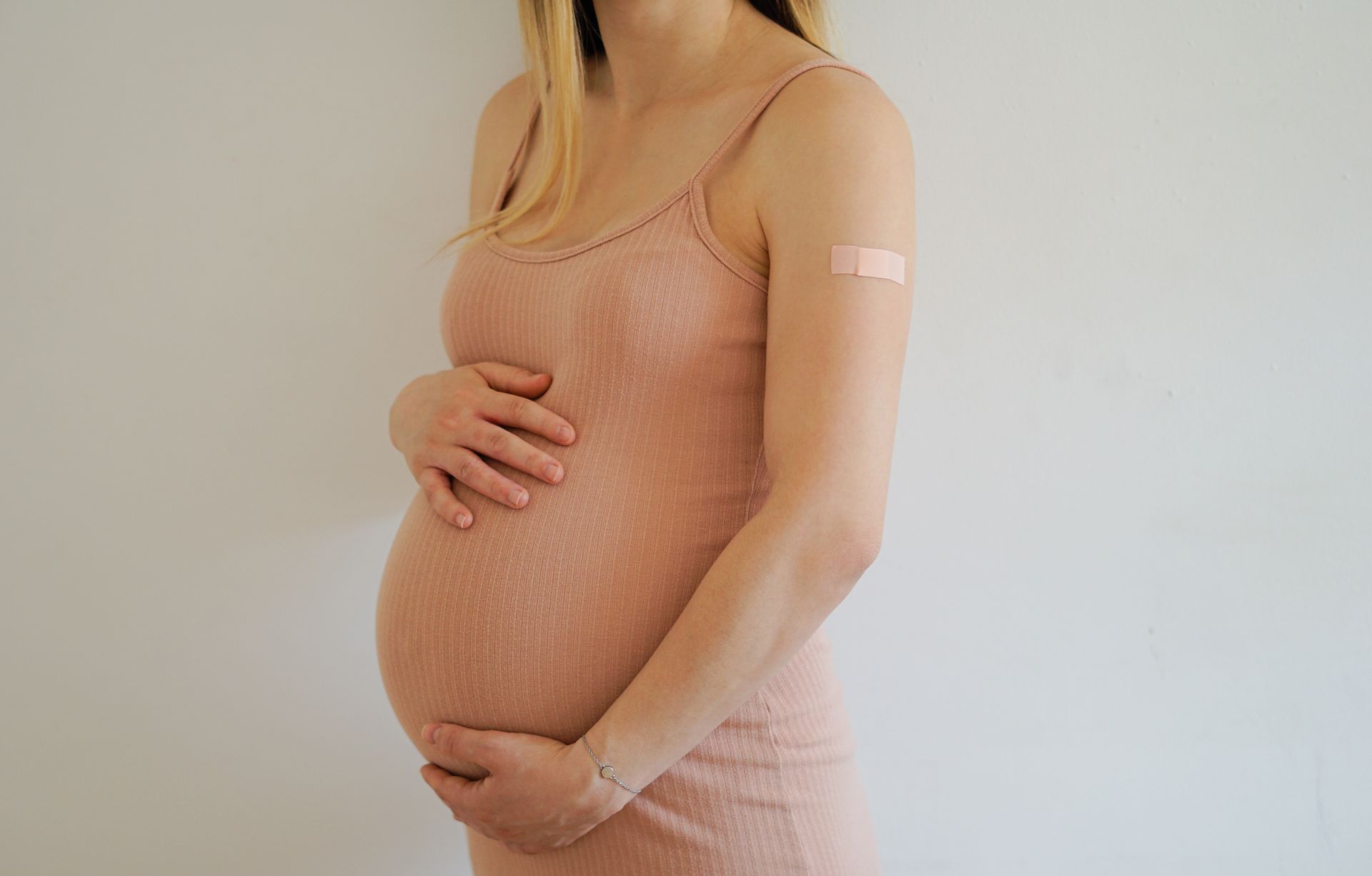 A pregnant woman is holding her belly and has a bandage on her arm.