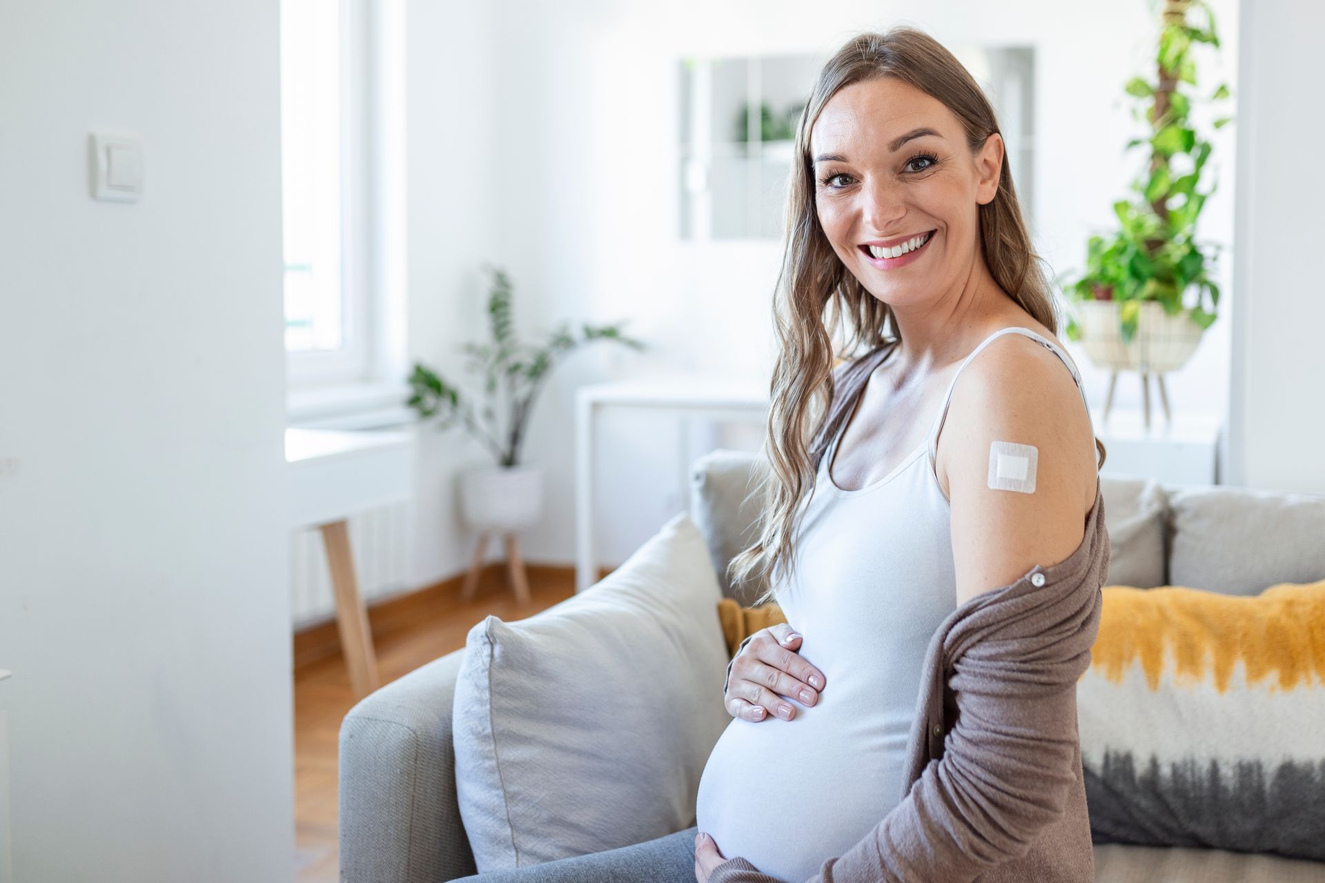 A pregnant woman is sitting on a couch with a bandage on her arm.