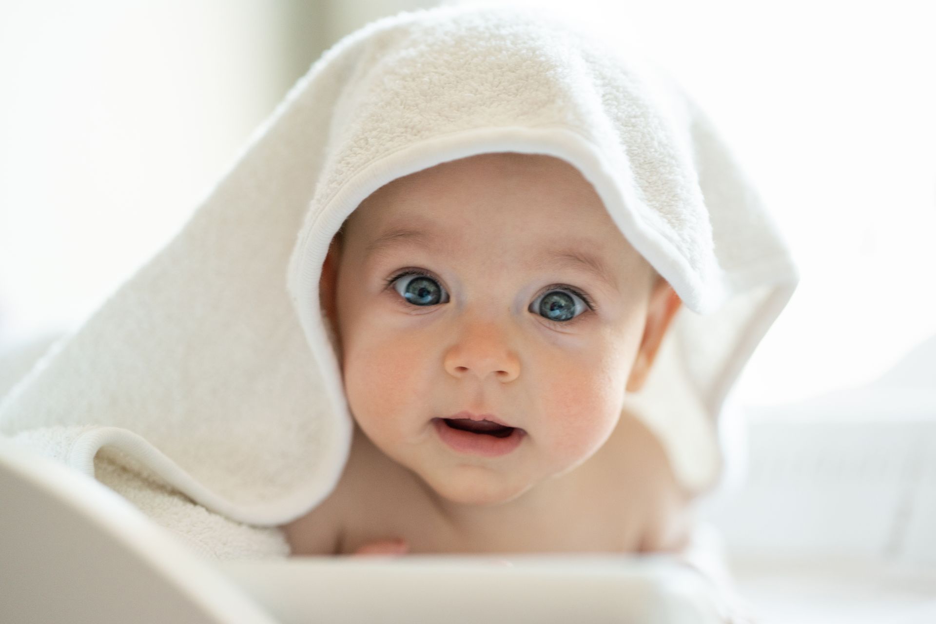 A baby is wrapped in a white towel and looking at the camera.