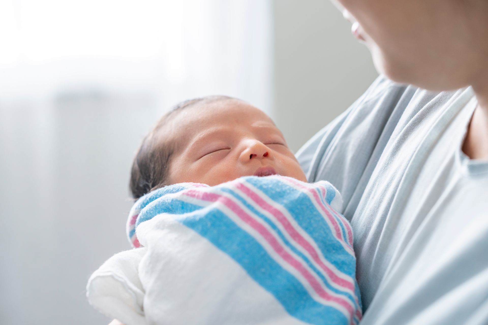 A woman is holding a newborn baby wrapped in a striped blanket.
