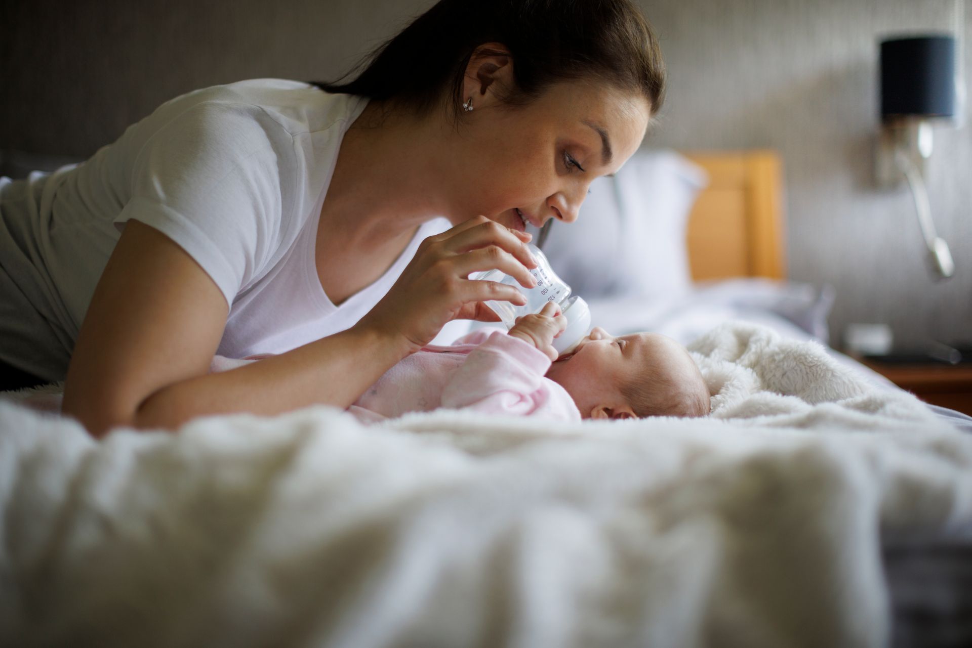 A woman is feeding her baby from a bottle on a bed.
