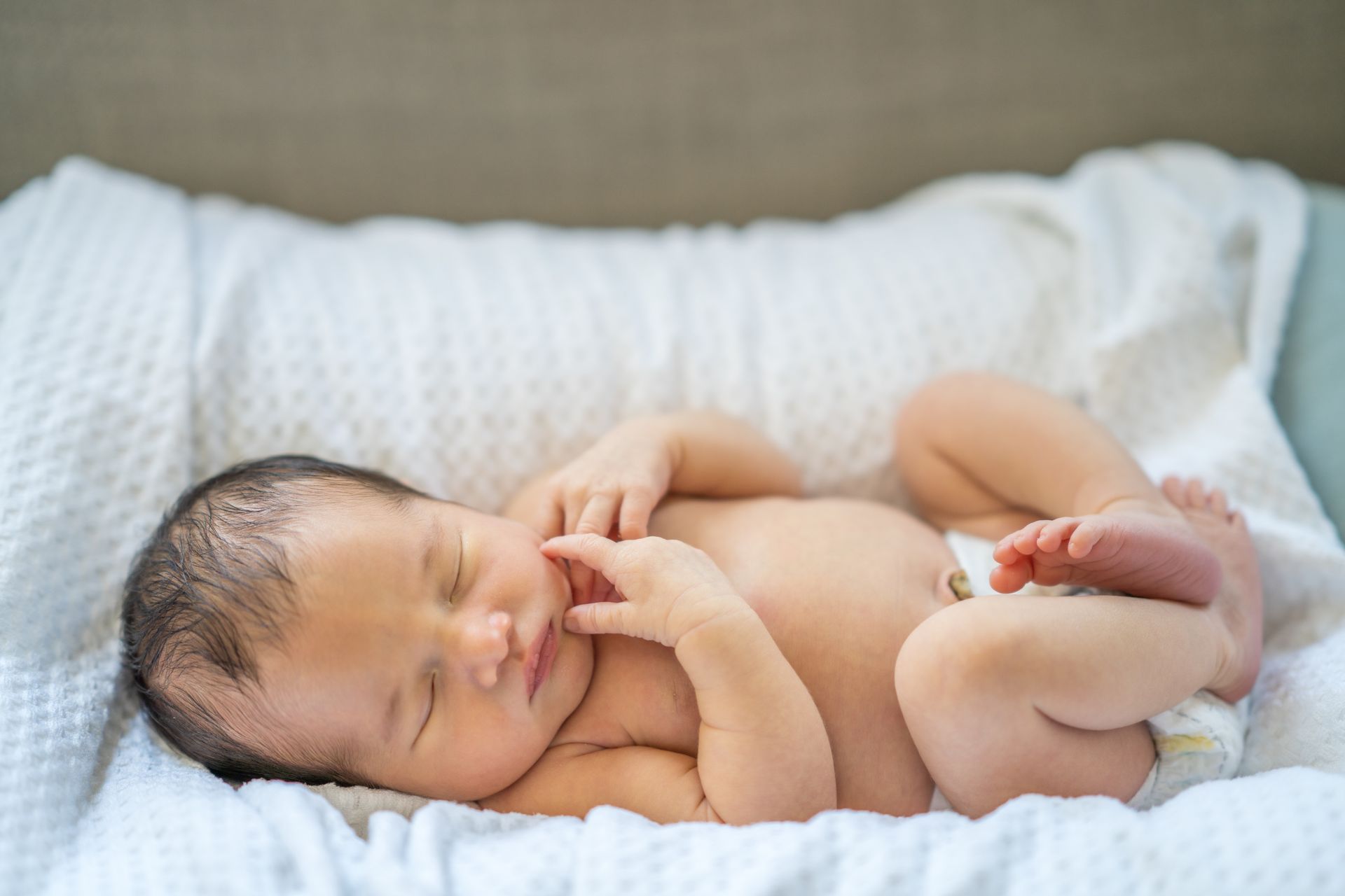 A newborn baby is sleeping on a bed with a diaper on.