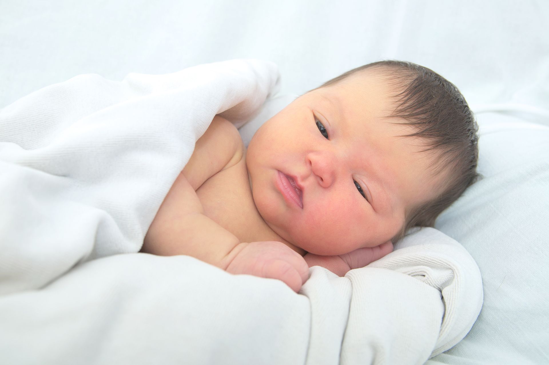 A newborn baby wrapped in a white blanket is sleeping on a bed.