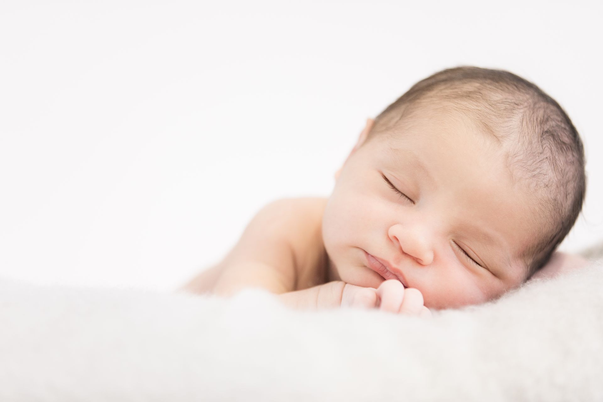 A newborn baby is sleeping on a white blanket.