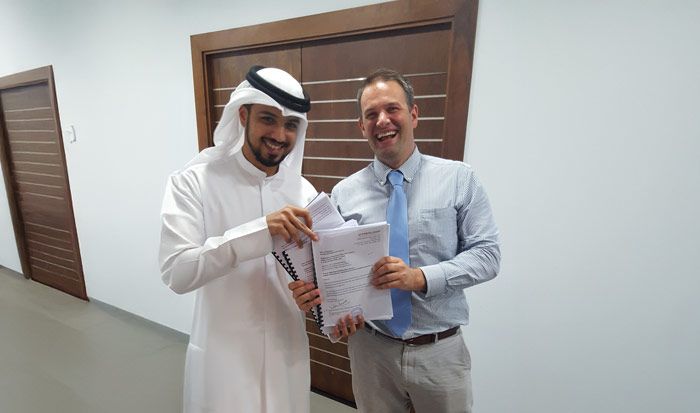 Two men are standing next to each other in a hallway holding papers.