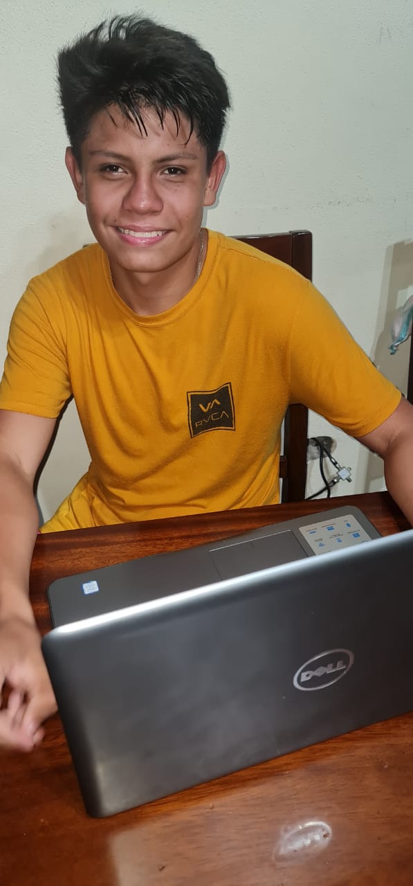 A young boy is sitting at a table with a laptop on it.