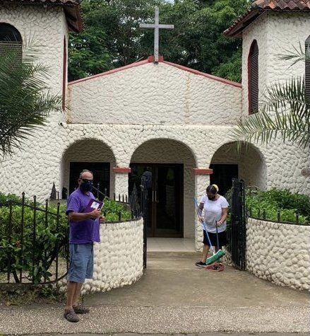 A man in a purple shirt is standing in front of a church.