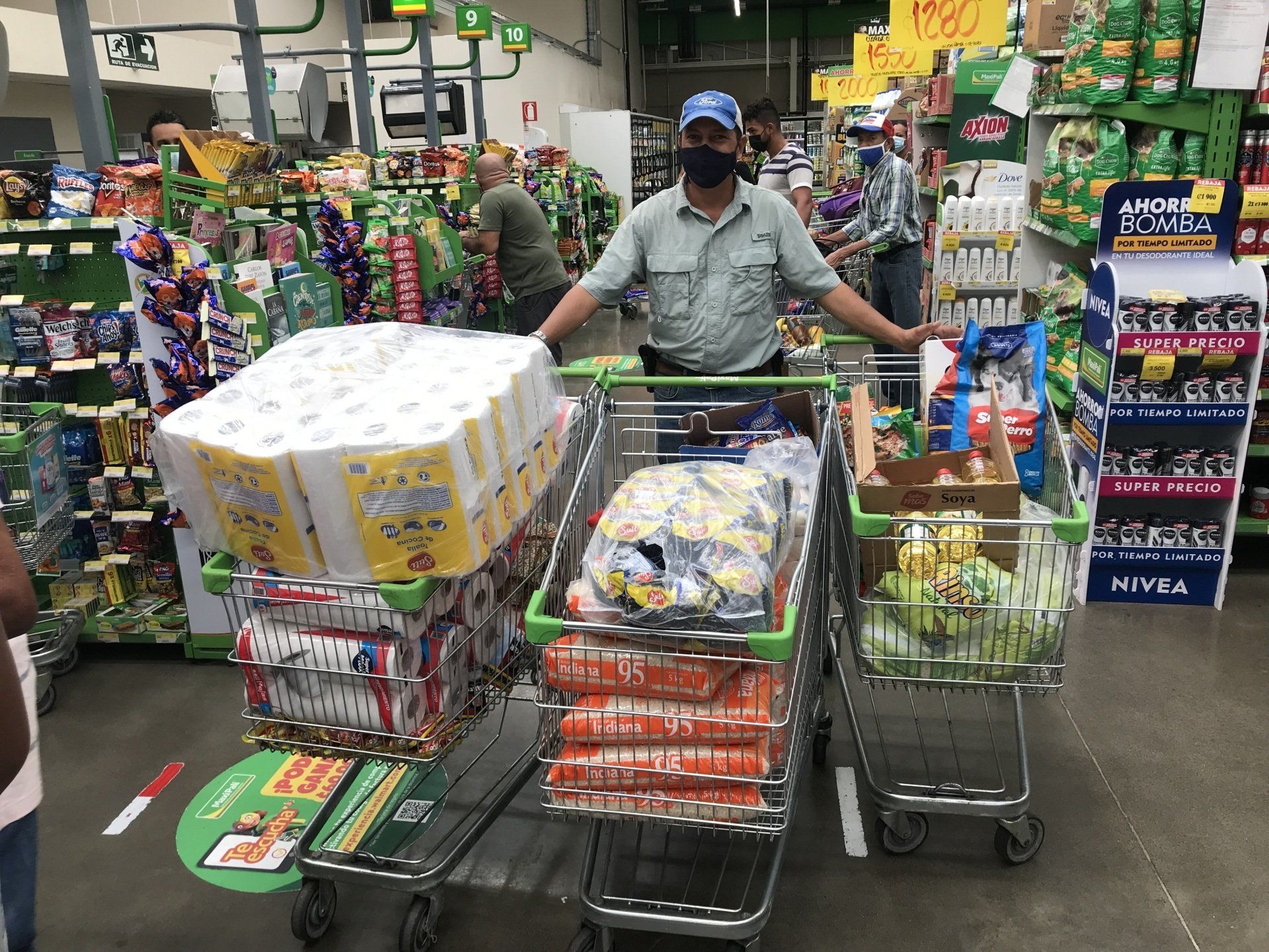 A man wearing a mask is pushing two shopping carts in a grocery store.