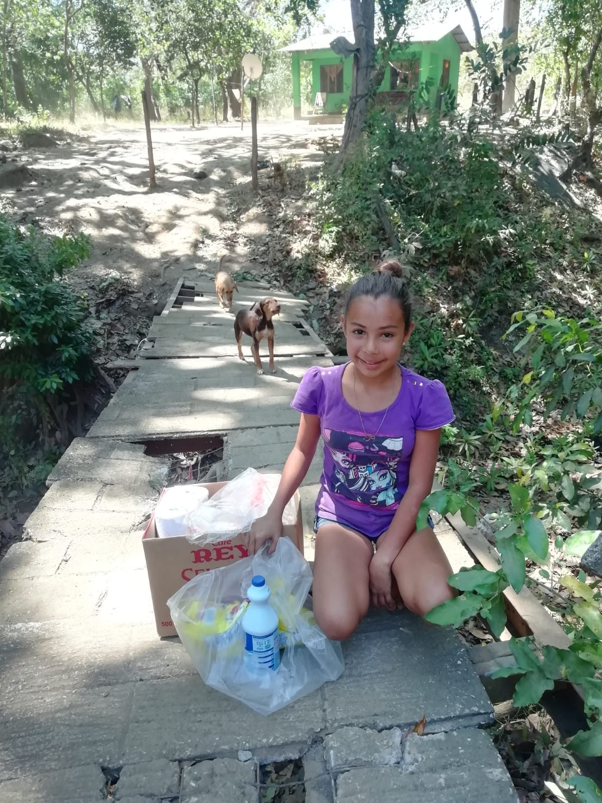 A little girl is sitting on a bridge next to a box and a bottle of water.