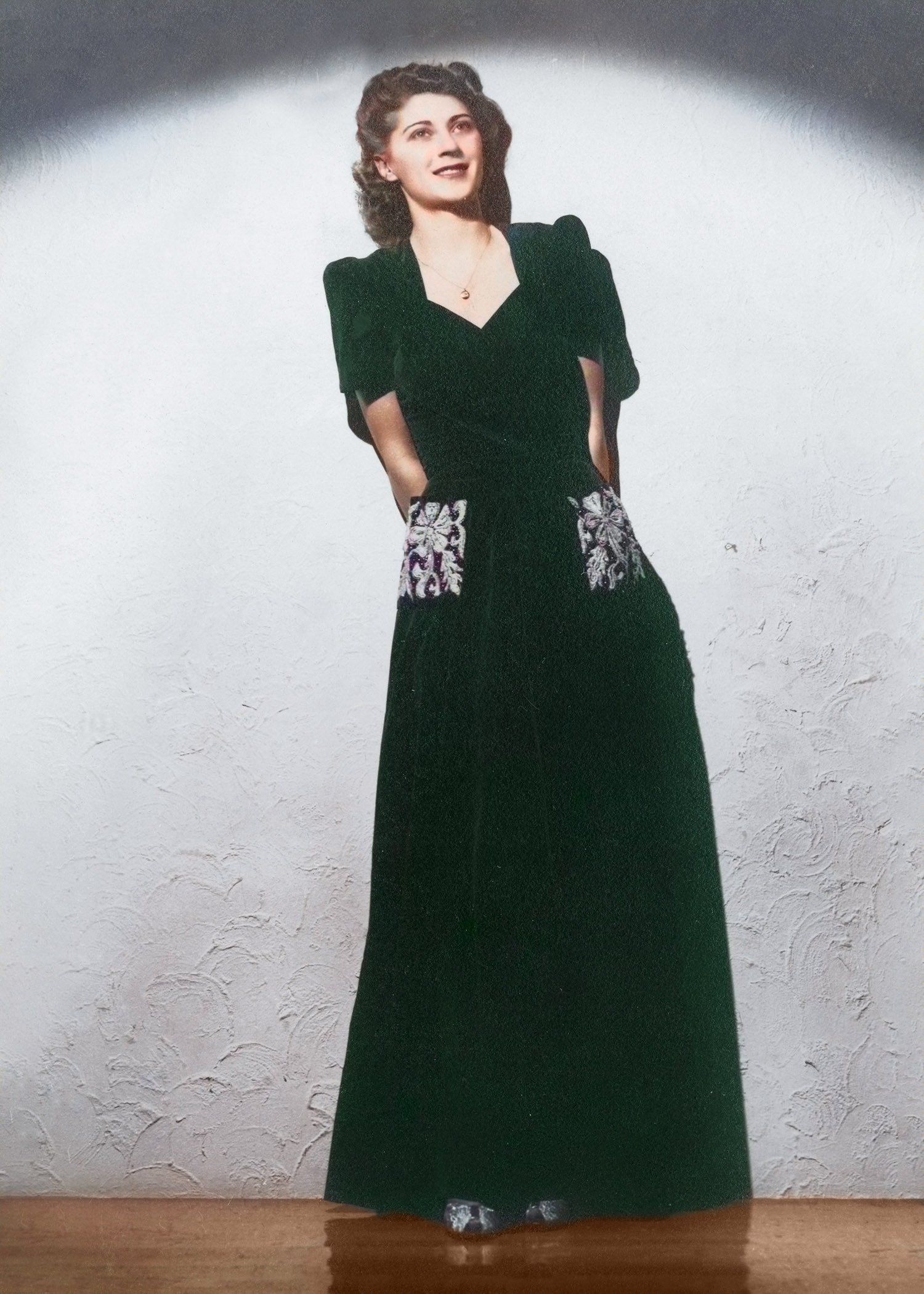 A woman in a long green dress is standing in front of a wall