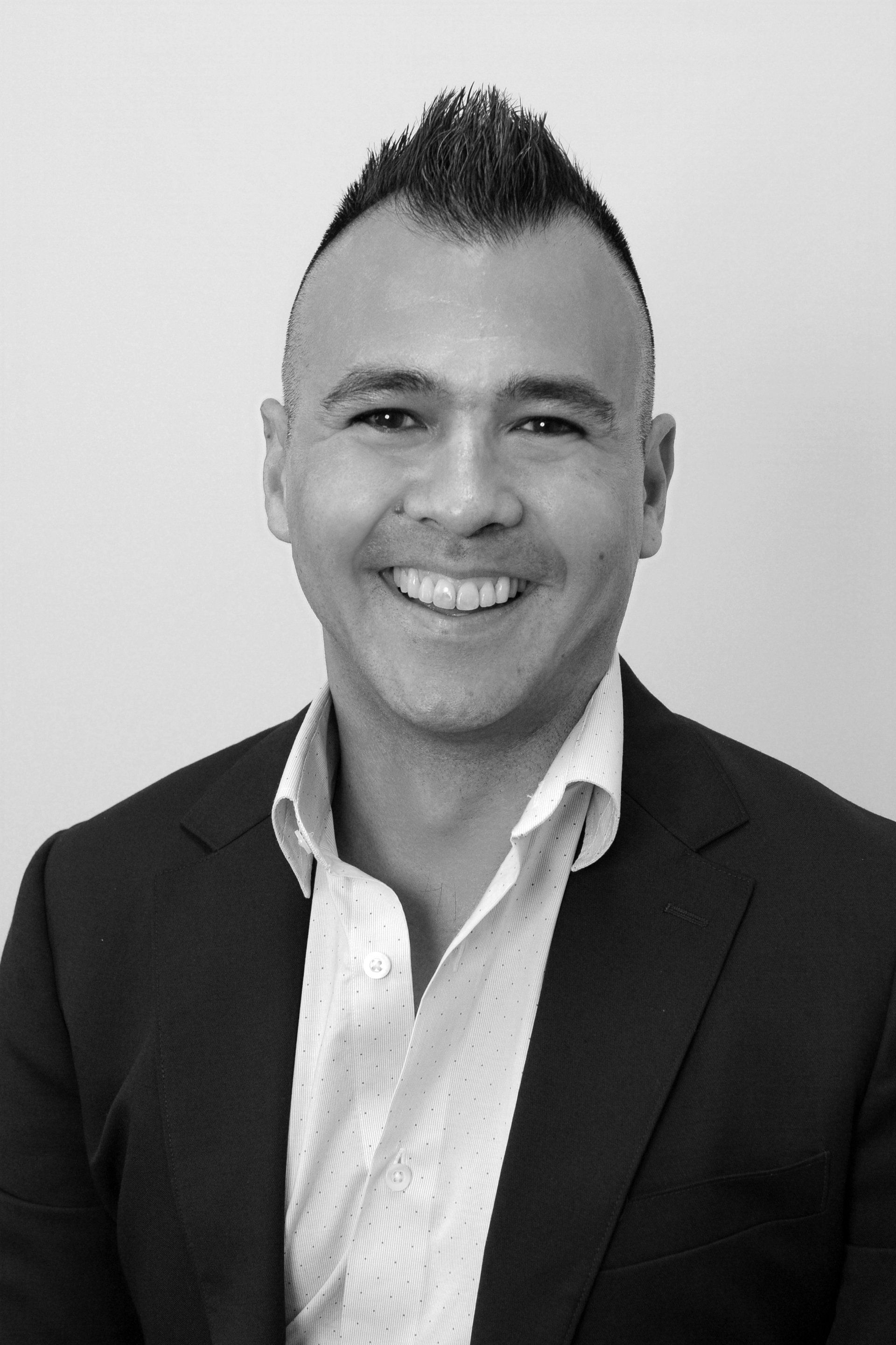 A man in a suit and white shirt is smiling in a black and white photo.