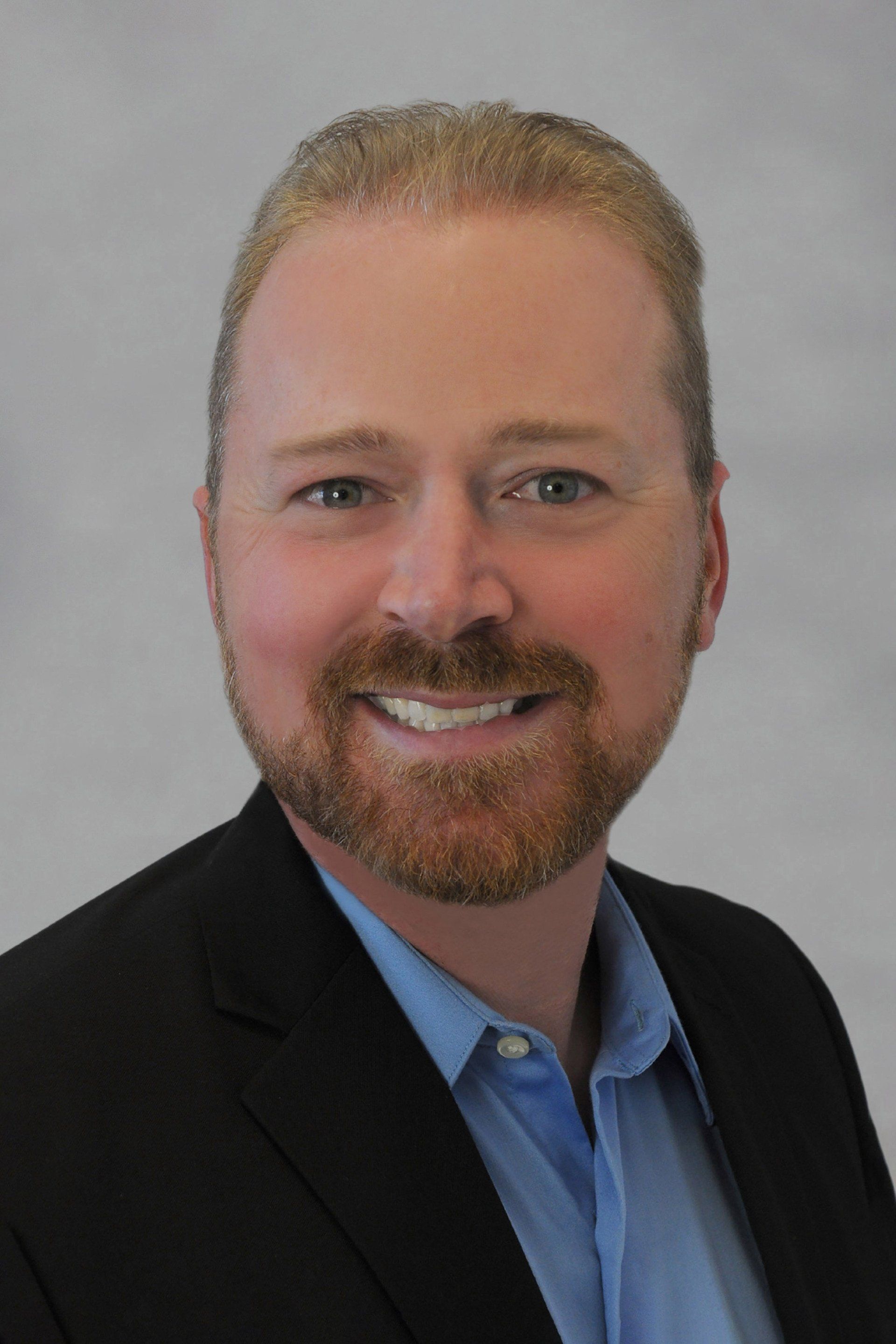 A man with a beard is wearing a suit and smiling for the camera.
