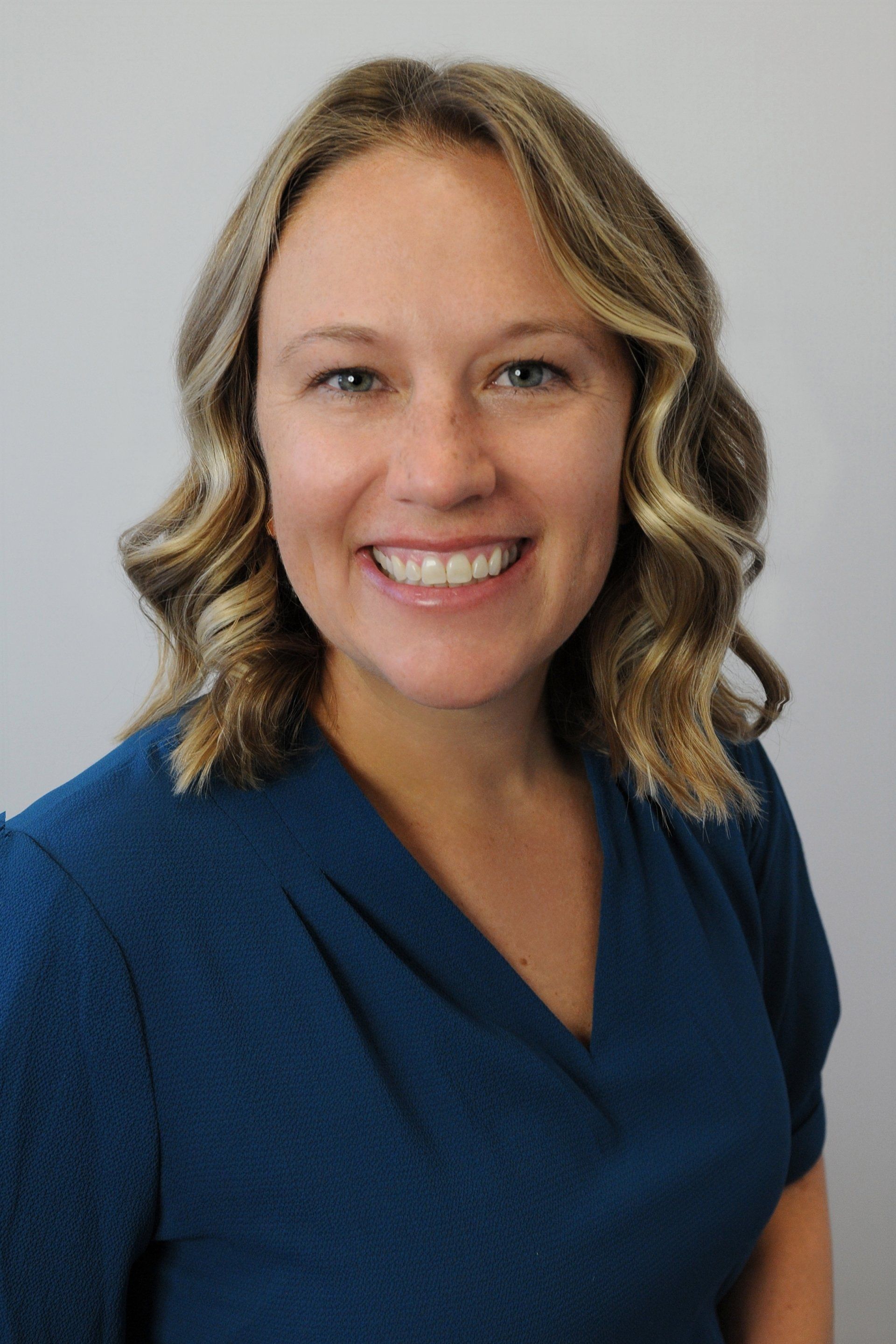A woman in a blue shirt is smiling for the camera.