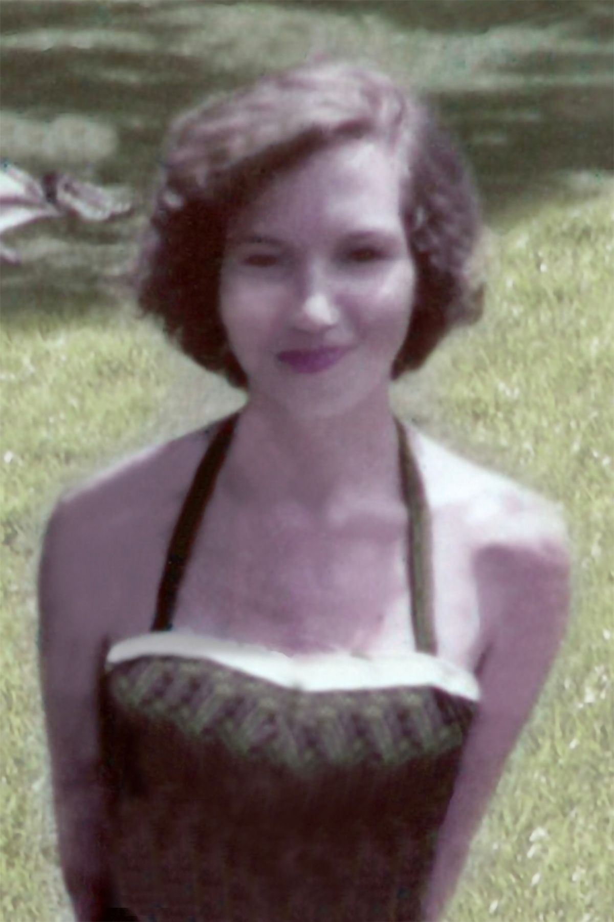A woman in a dress is standing in the grass and smiling.