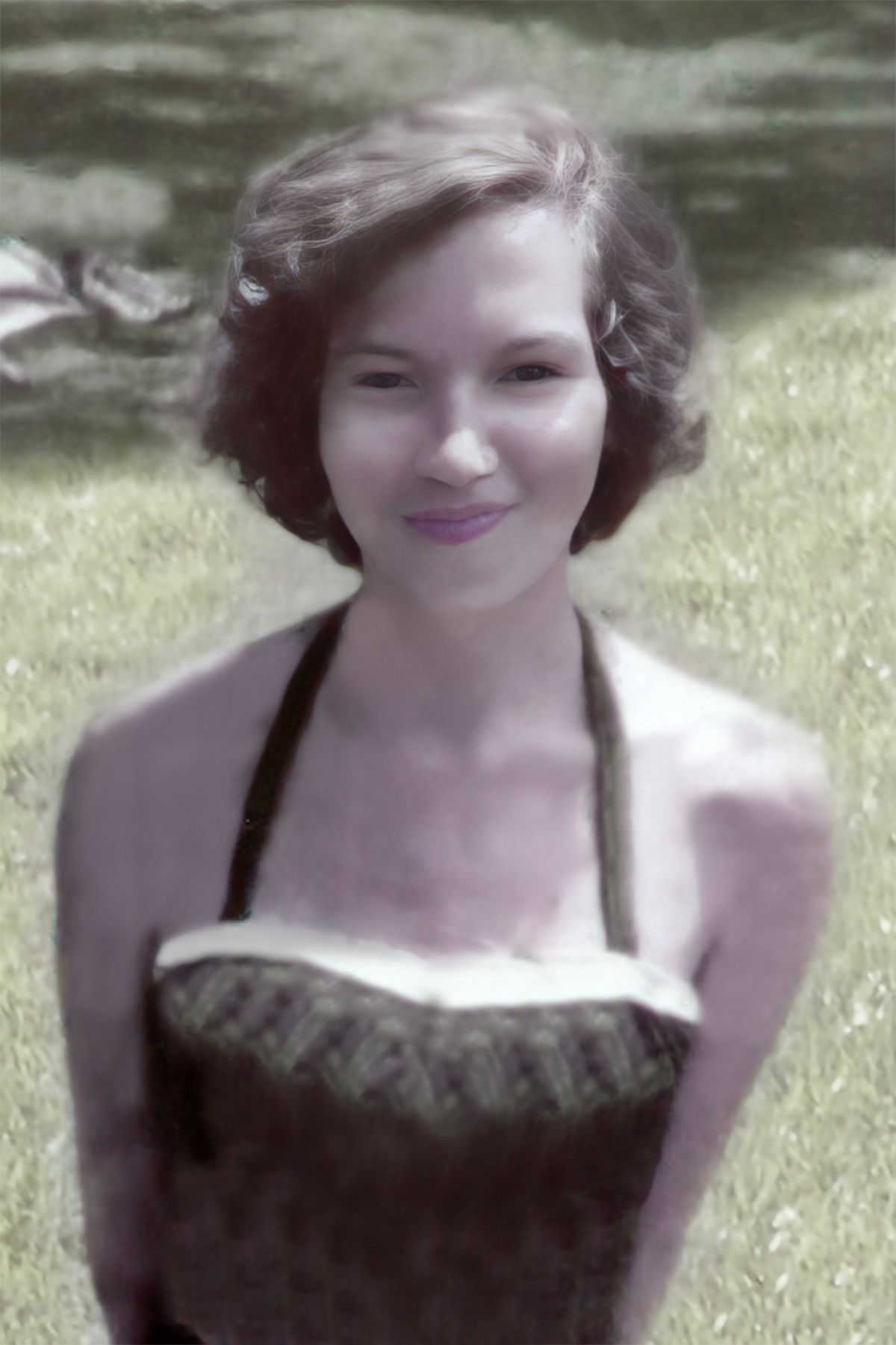 A woman in a black dress is standing in the grass and smiling.