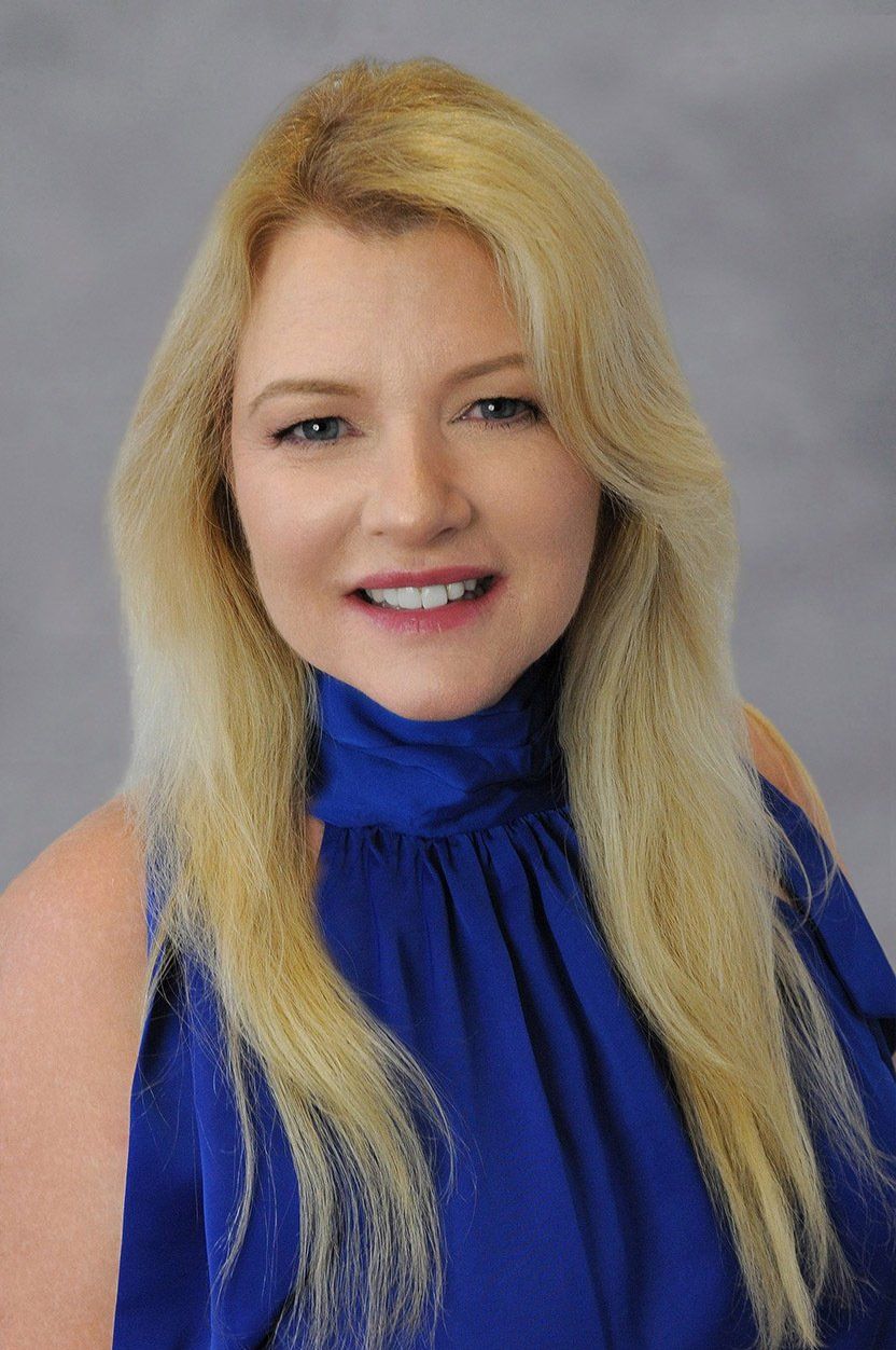 The woman is wearing a blue top and smiling for the camera.