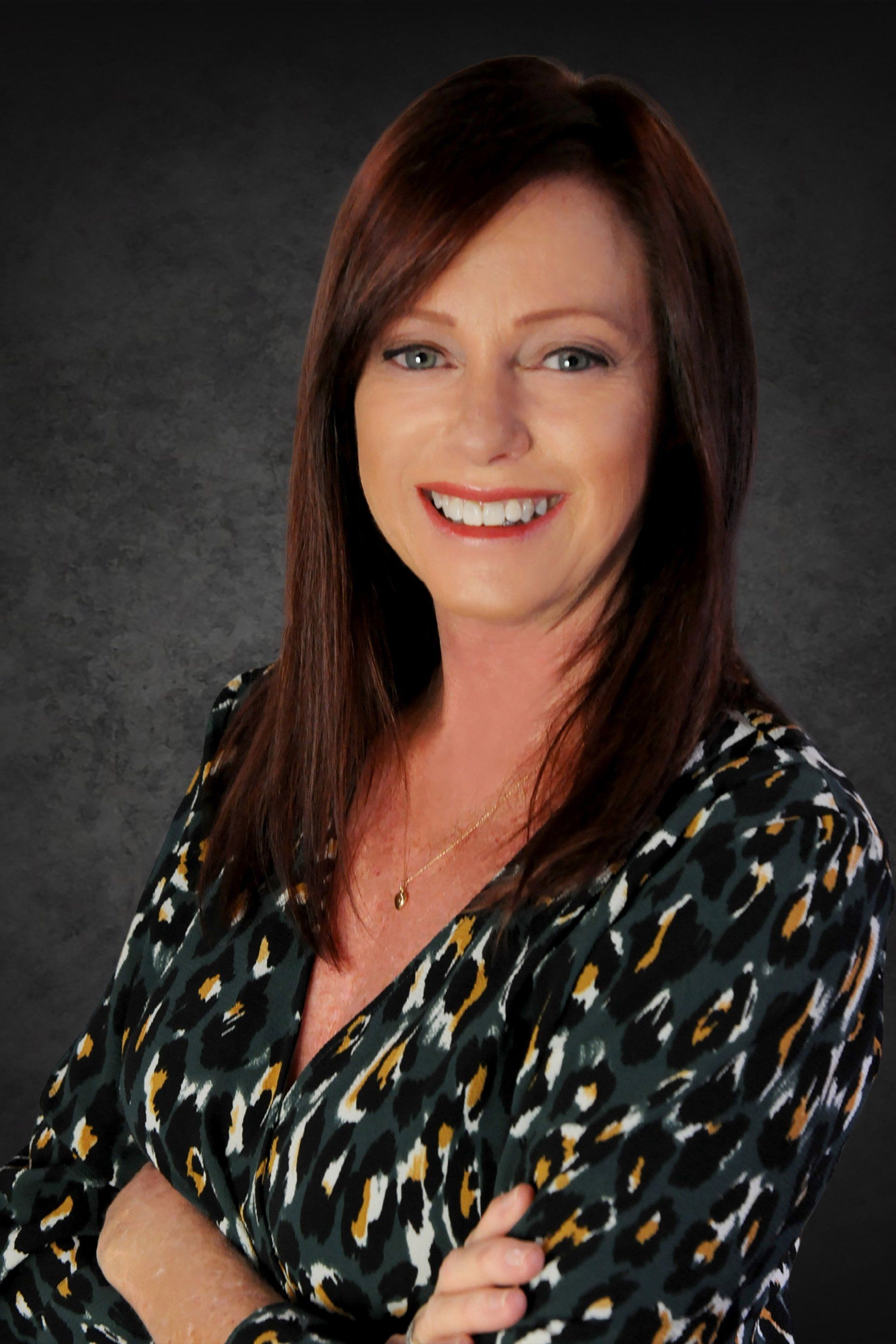 A woman in a leopard print shirt is smiling with her arms crossed.