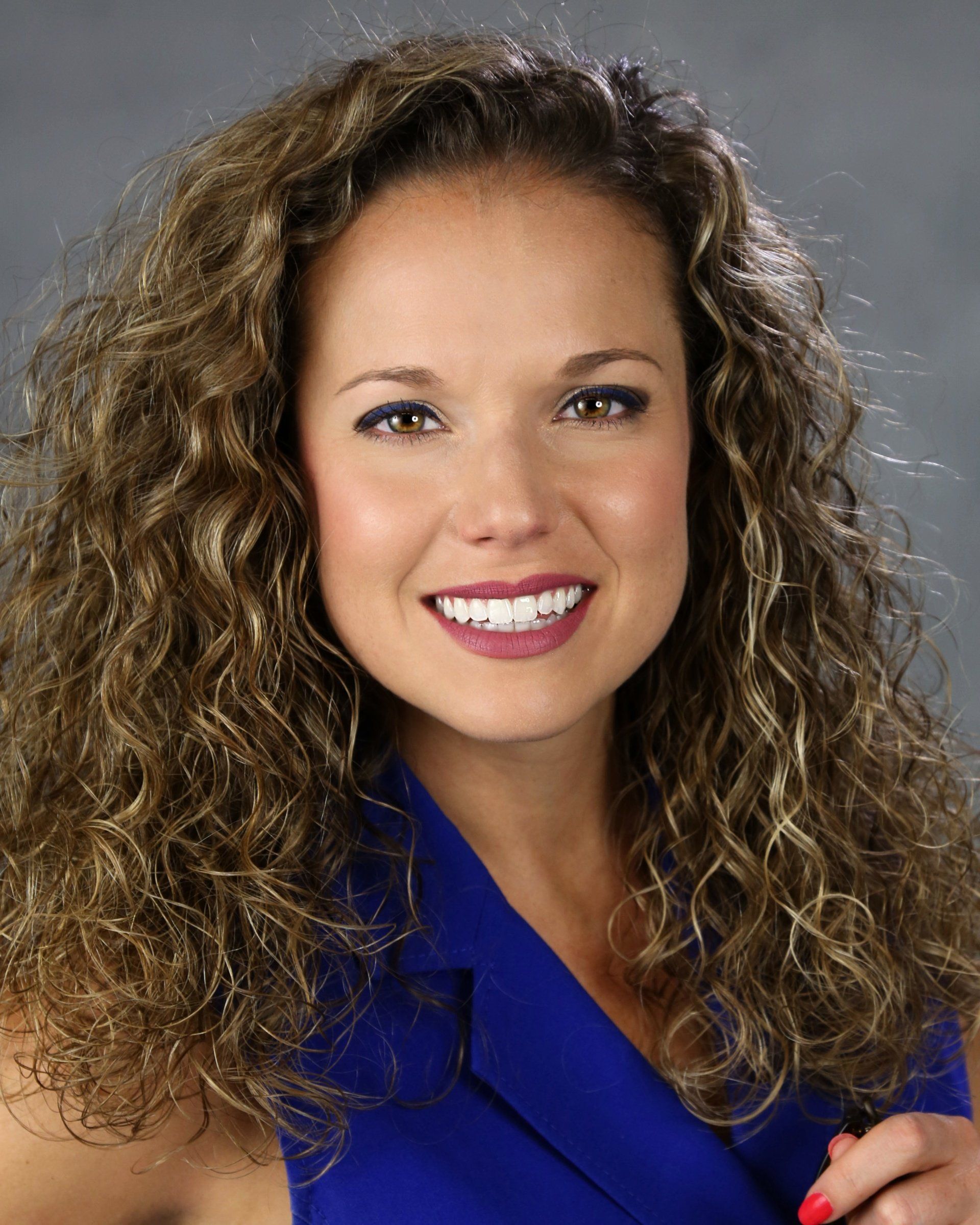 A woman with curly hair is wearing a blue shirt and smiling