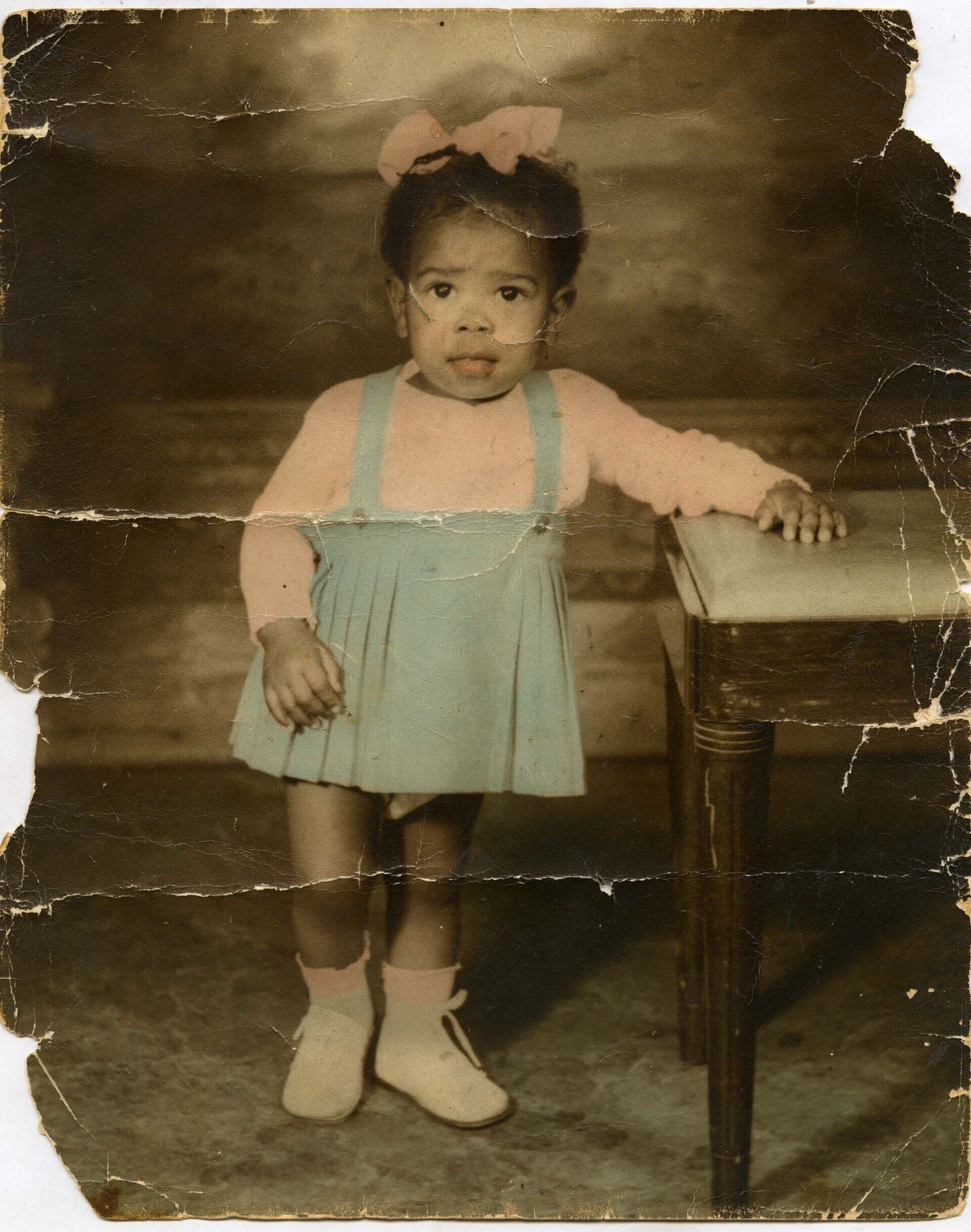 A little girl with a pink bow in her hair is standing next to a table
