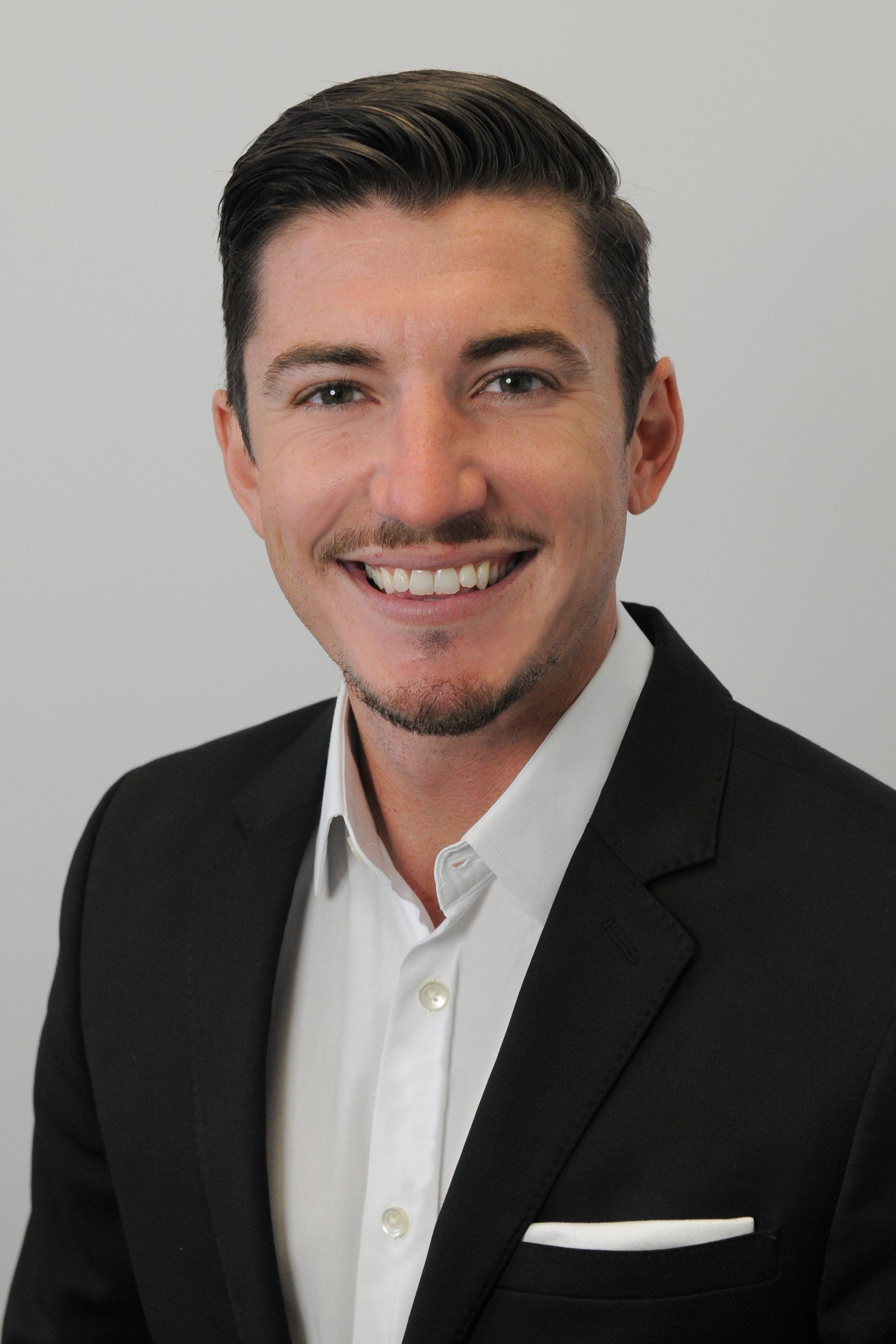 A man in a suit and white shirt is smiling for the camera.