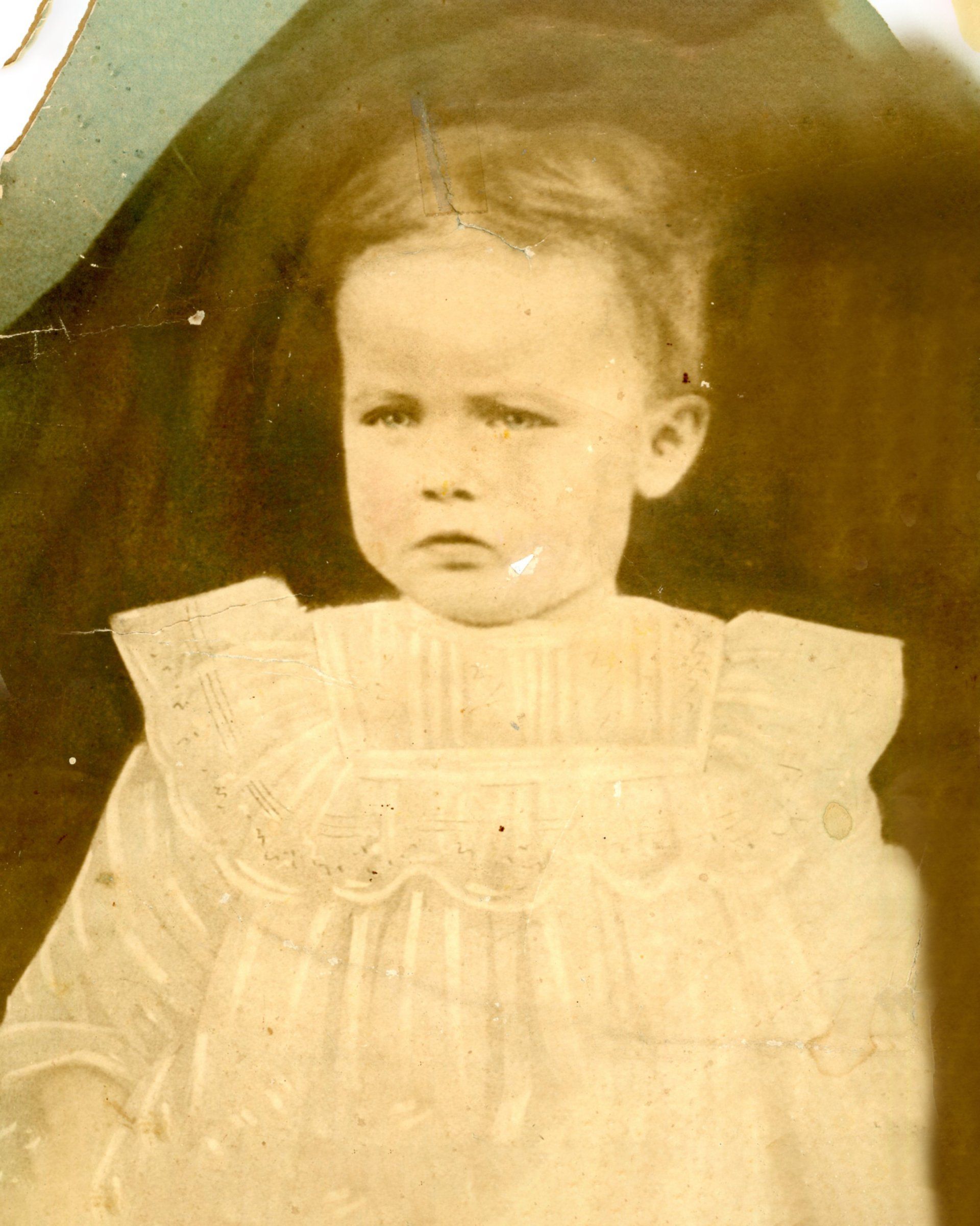 A black and white photo of a little girl in a white dress.