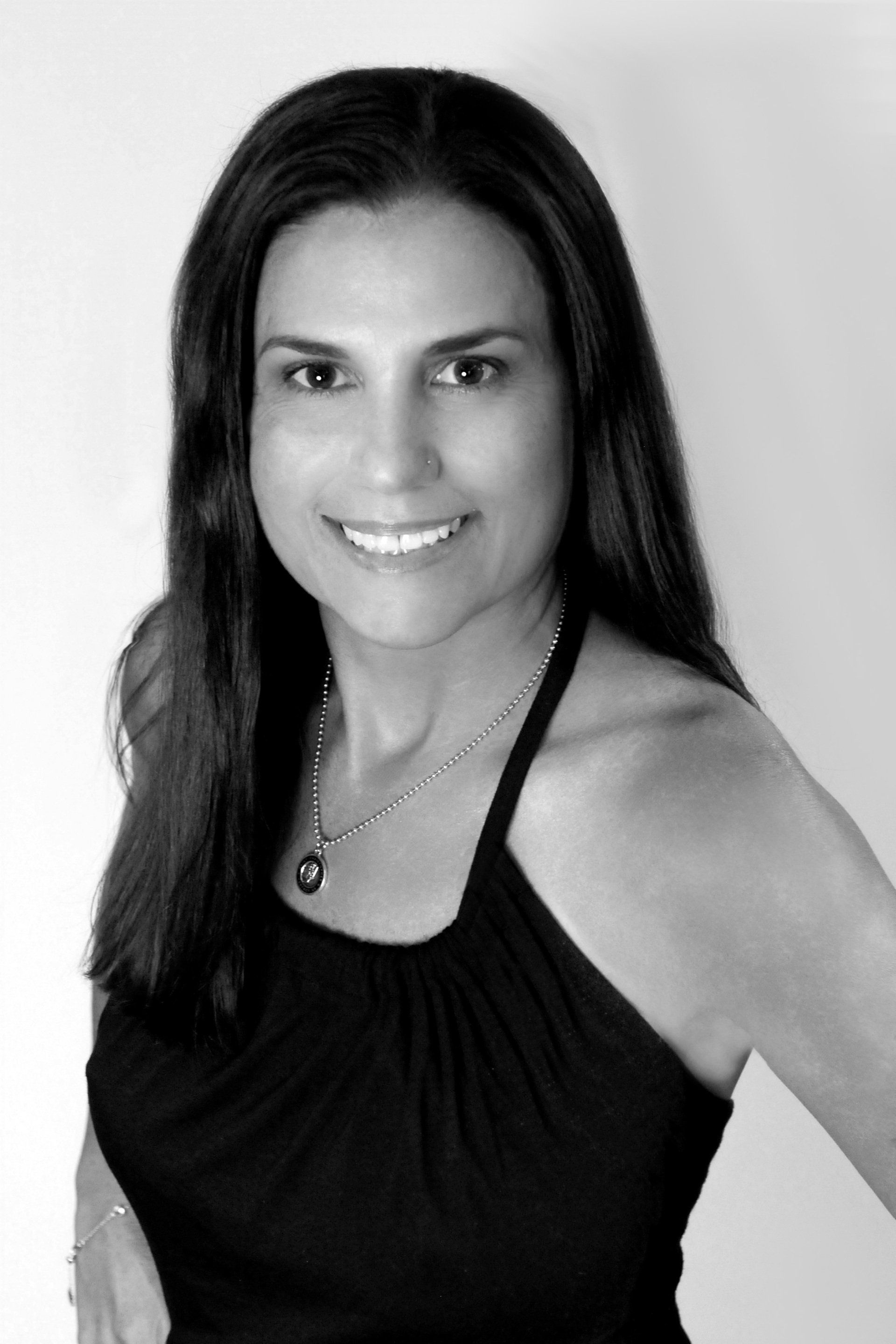 A woman in a black tank top and necklace is smiling in a black and white photo.