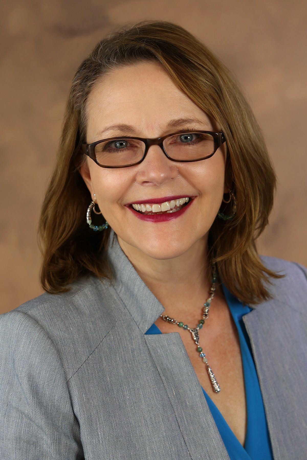 A woman wearing glasses and a blue shirt is smiling for the camera.