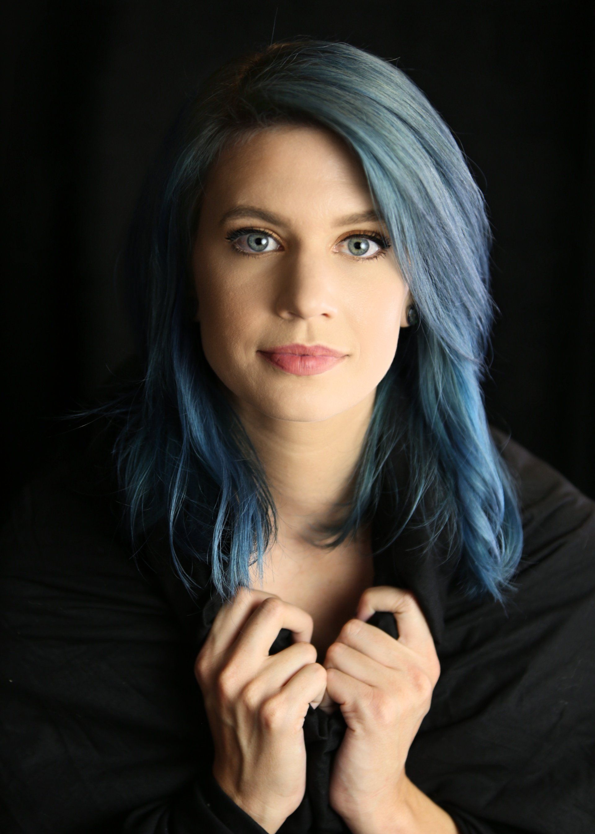 A woman with blue hair and blue eyes is wearing a black shirt.