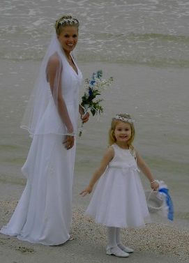 A bride and her flower girl are posing for a picture on the beach.