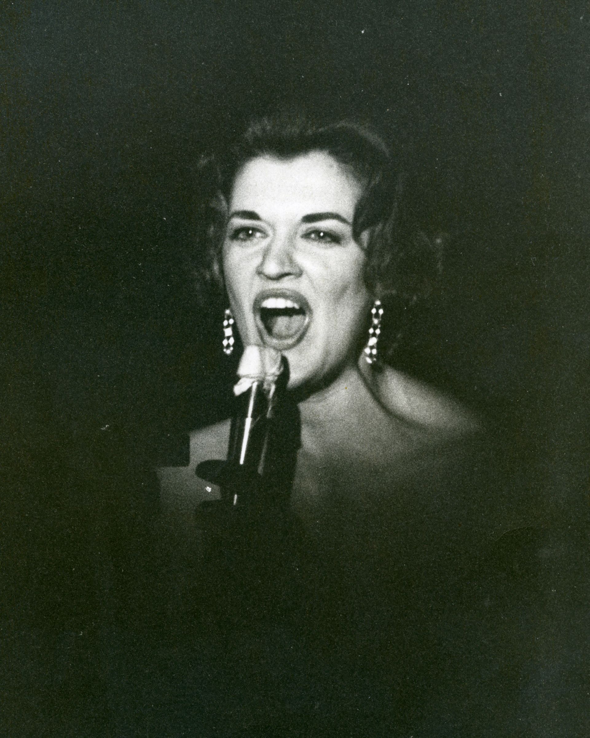 A black and white photo of a woman singing into a microphone
