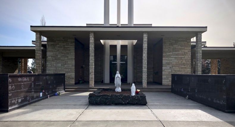 A stone mausoleum entrance with a central courtyard, featuring two religious statues, a cross, and granite wall niches.